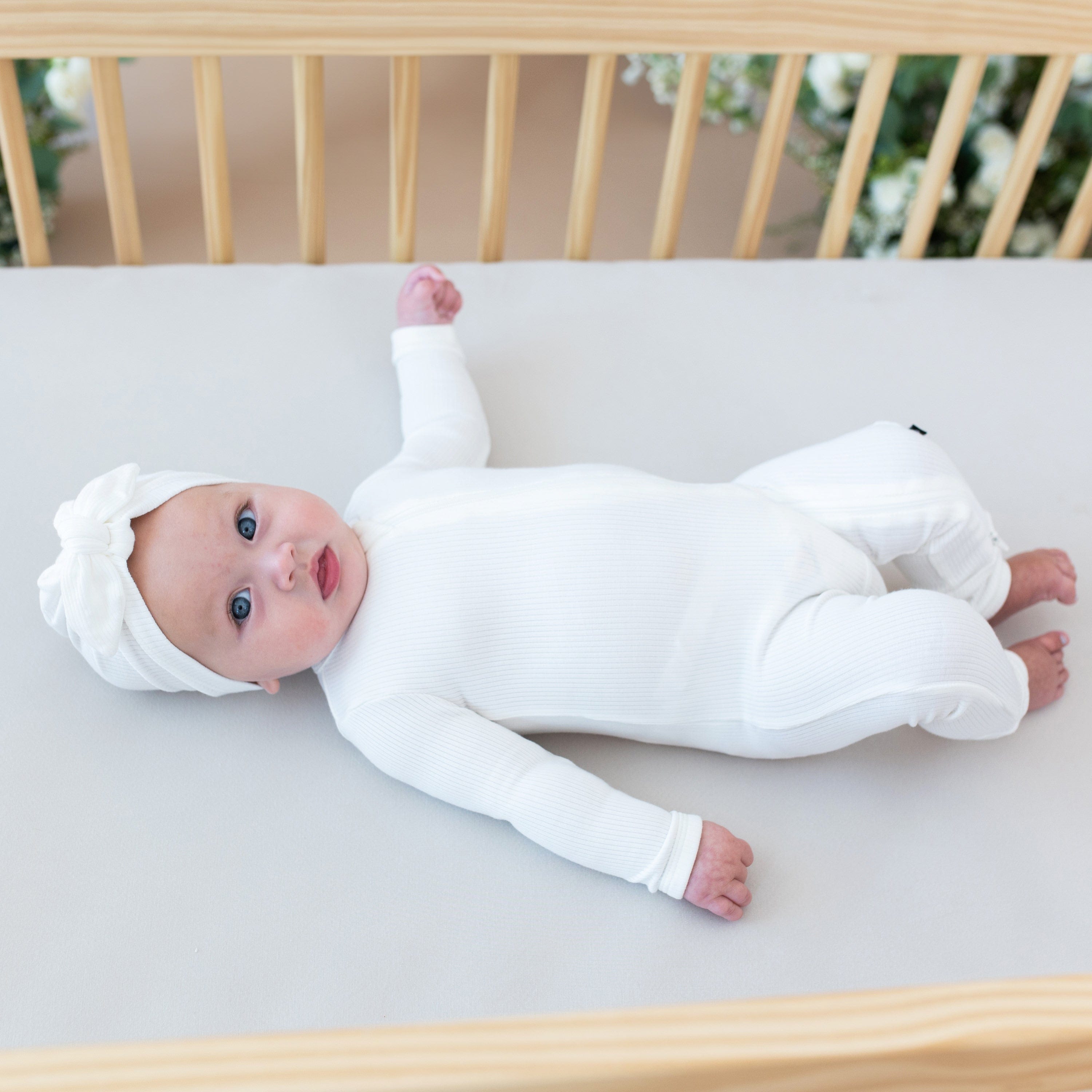 Infant laying in crib wearing Kyte Baby Ribbed Zippered Romper in Cloud
