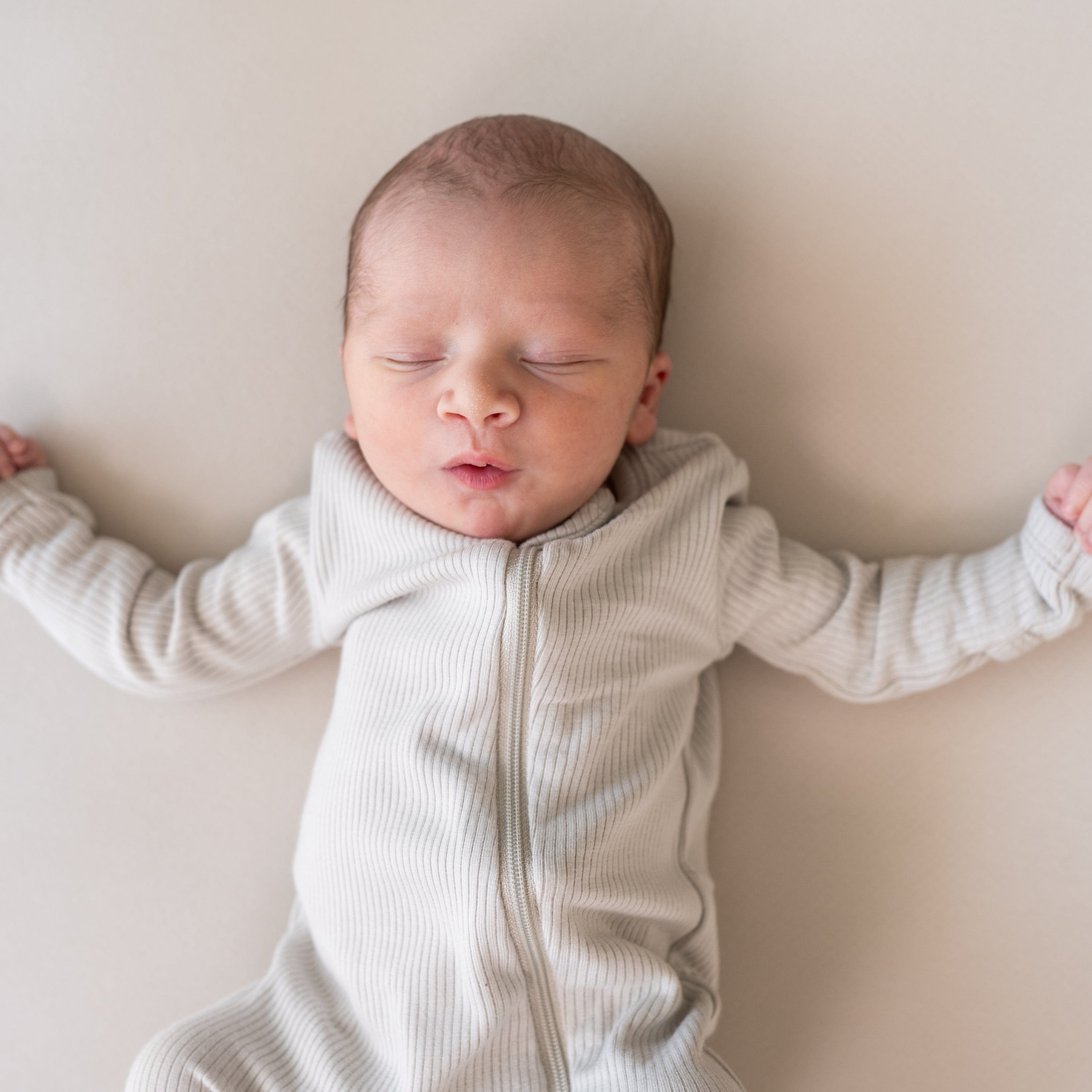 Newborn sleeping in Kyte Baby Ribbed Zippered Romper in Oat