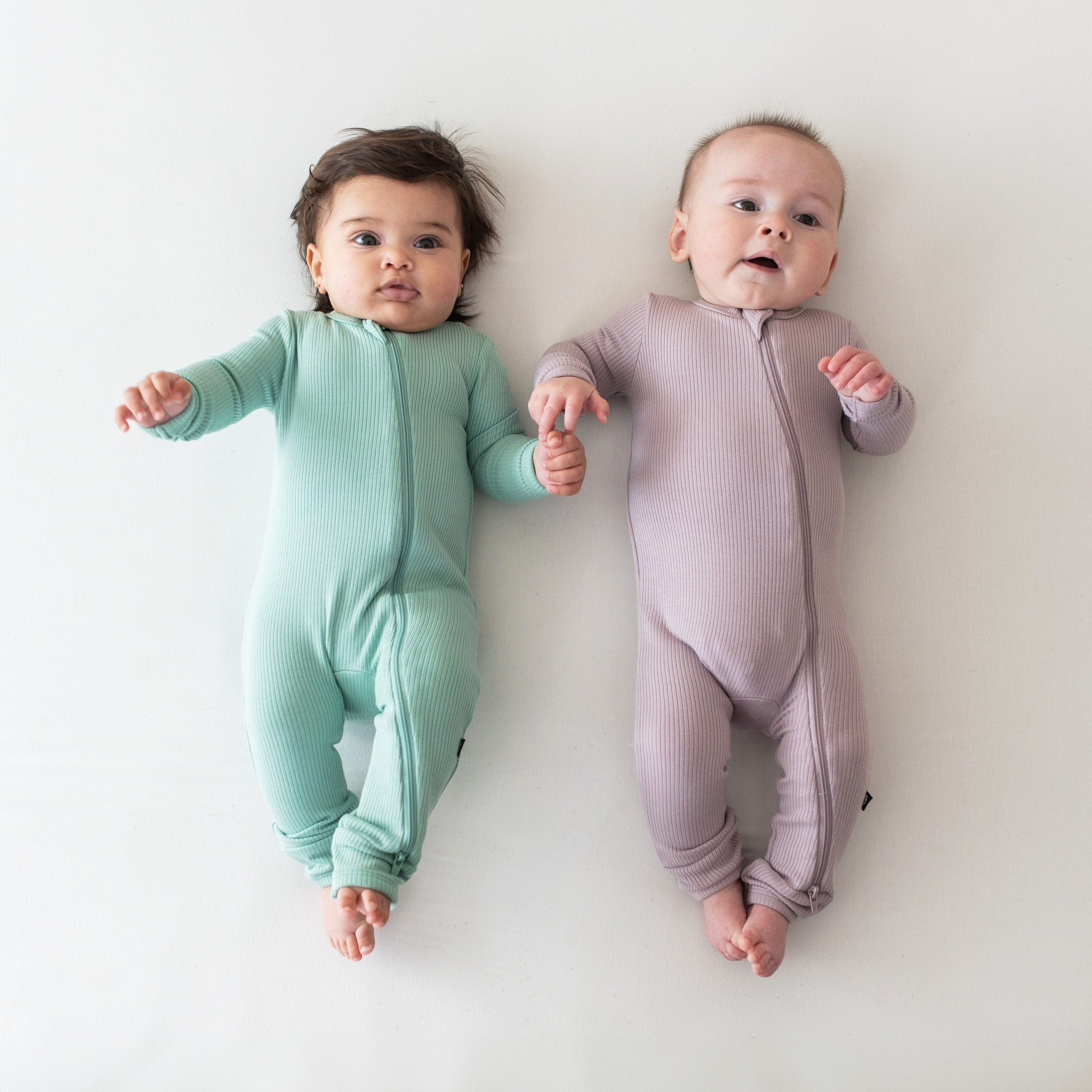 Infants wearing Kyte Baby bamboo Ribbed Zippered Romper pajamas