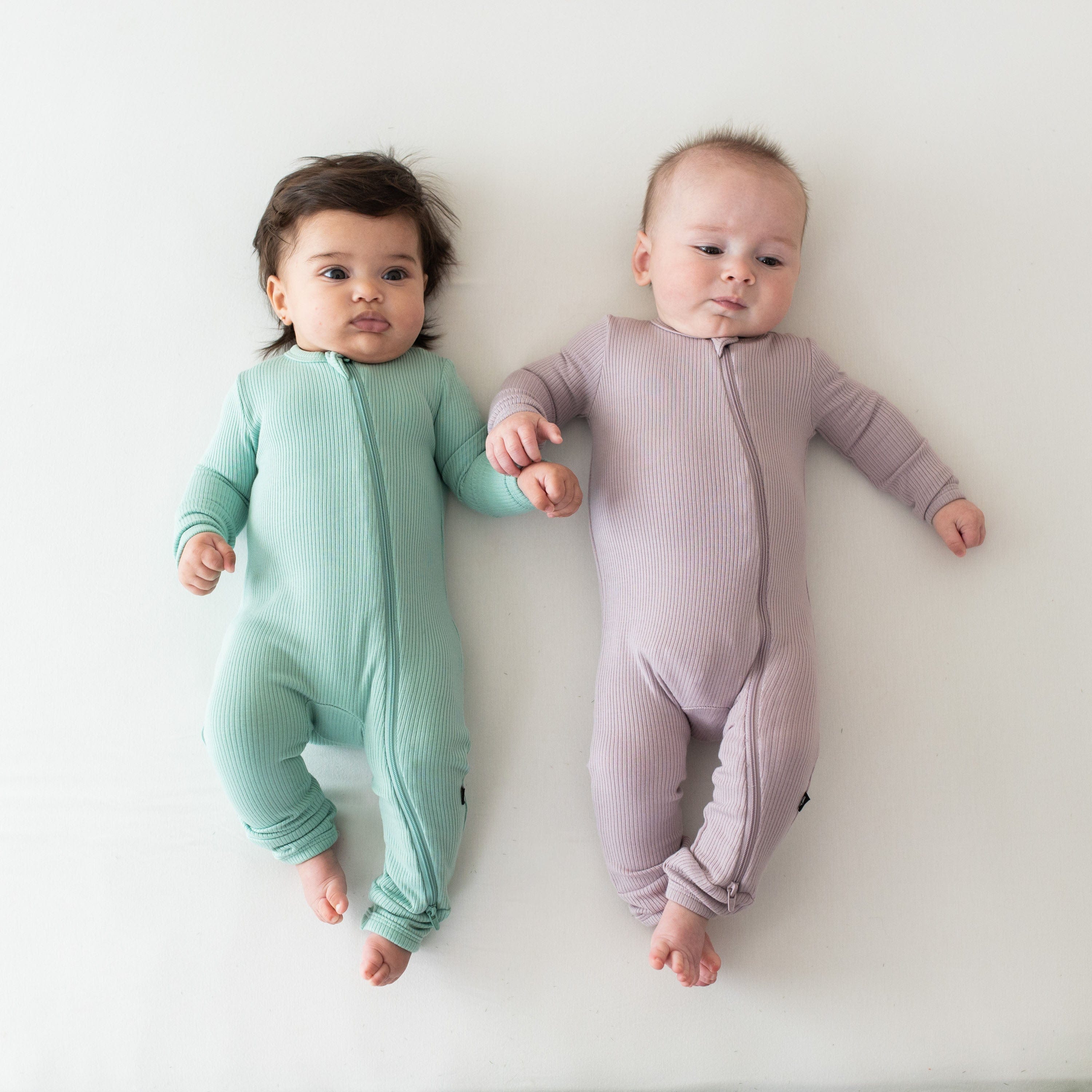 Infants wearing Kyte Baby bamboo Ribbed Zippered Rompers