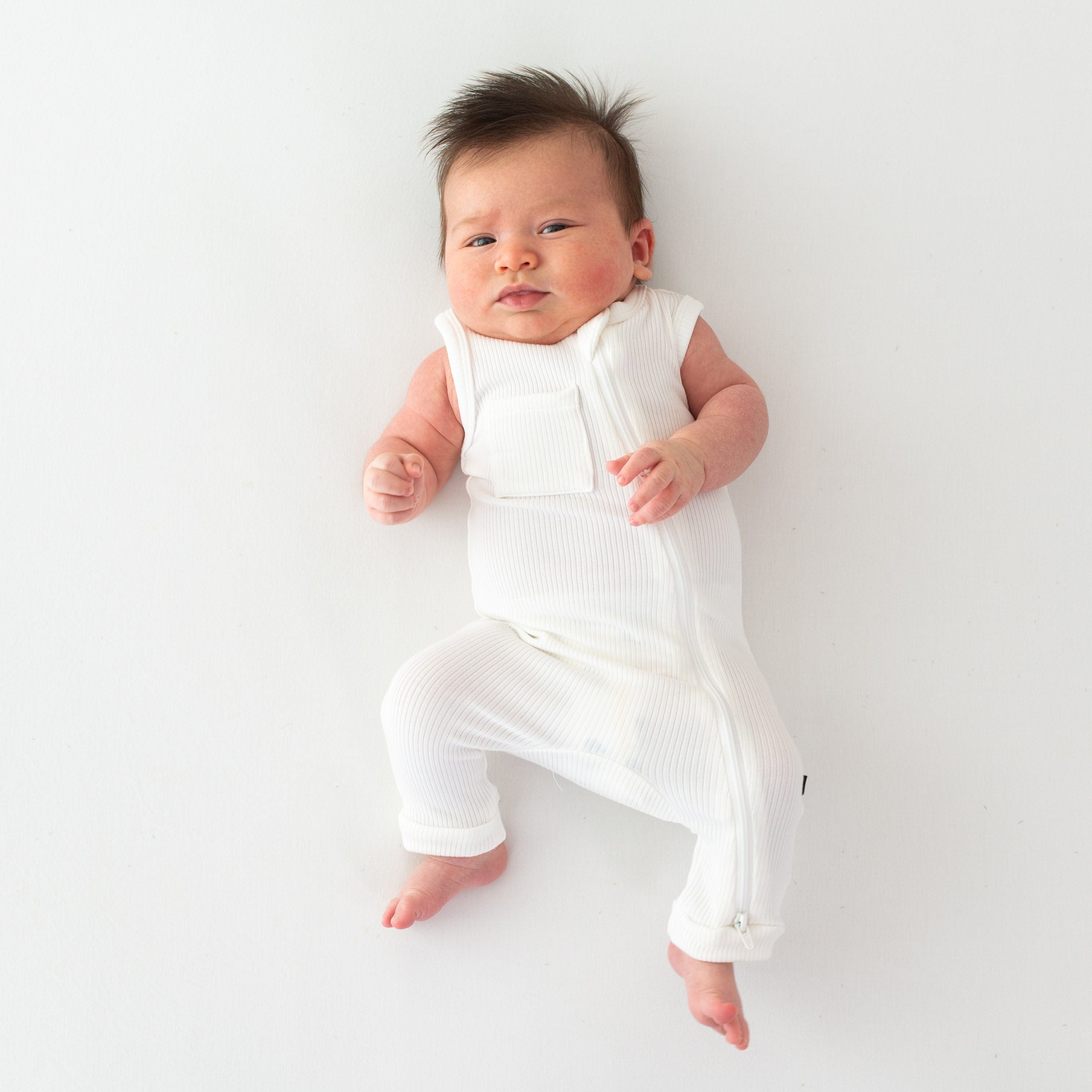 Infant wearing Kyte Baby Ribbed Zippered Sleeveless Romper in Cloud white