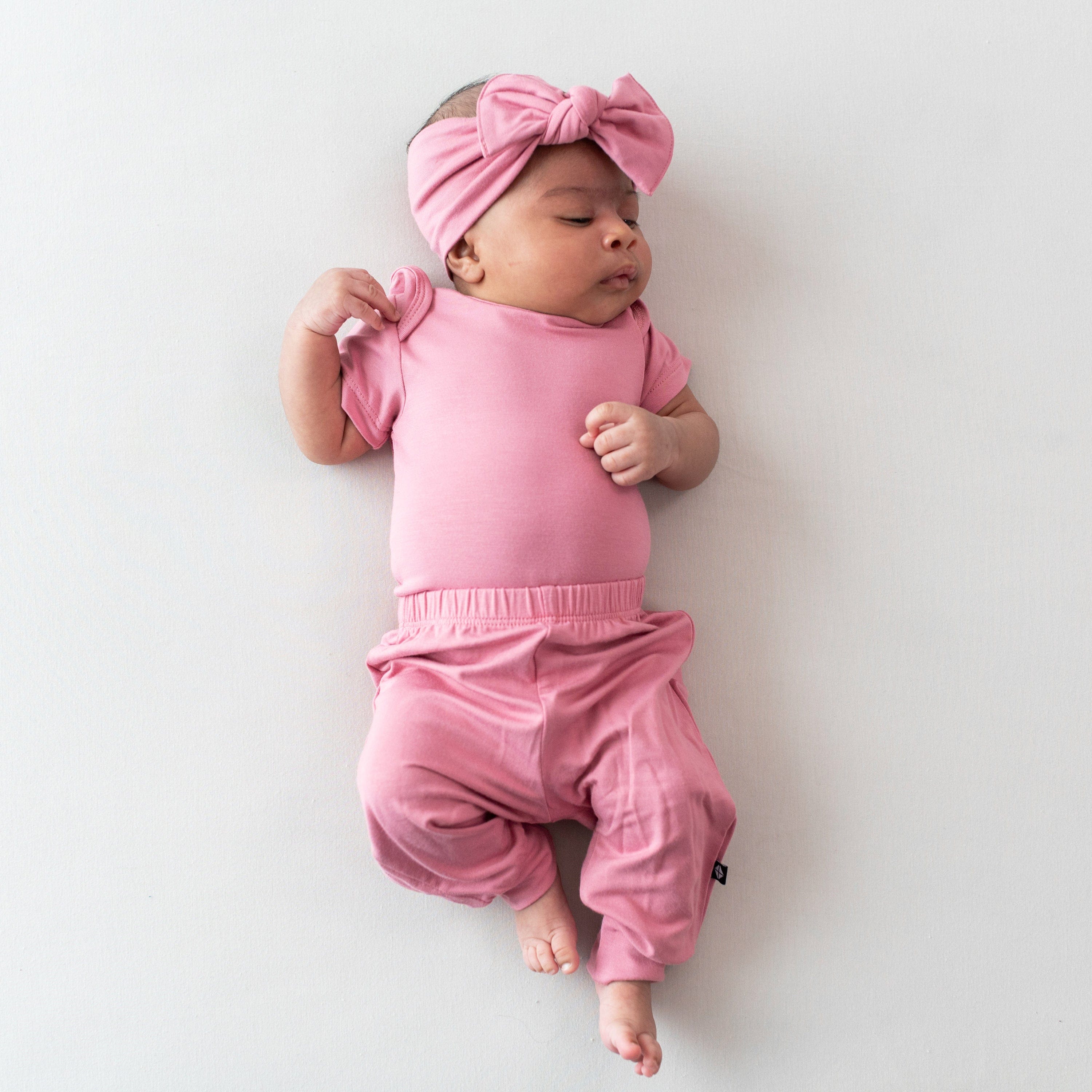 Infant wearing short sleeve onesie with pink baby pants and knotted bow headband in Apple Blossom