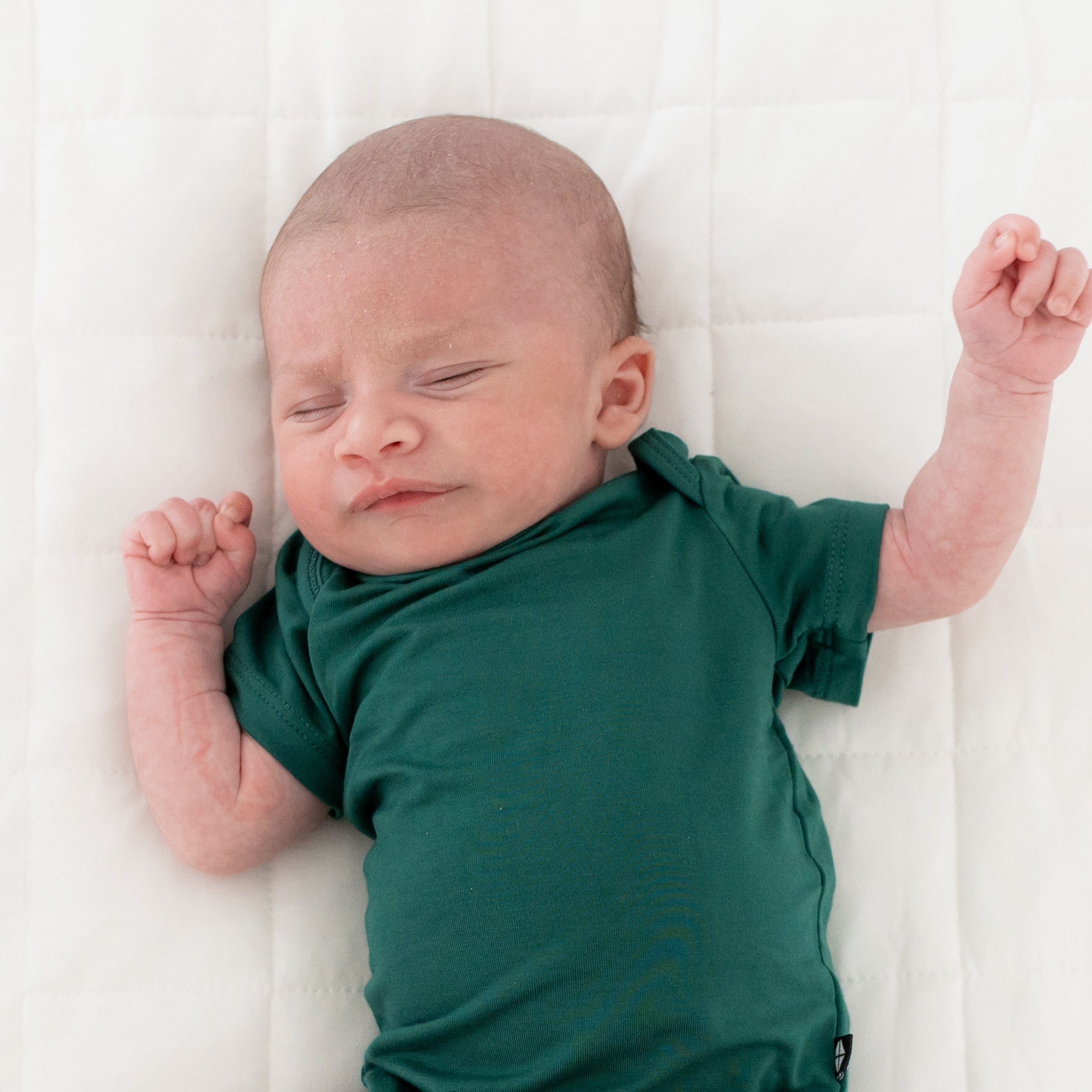Newborn wearing Kyte Baby Bodysuit in Emerald while laying on a Cloud Blanket