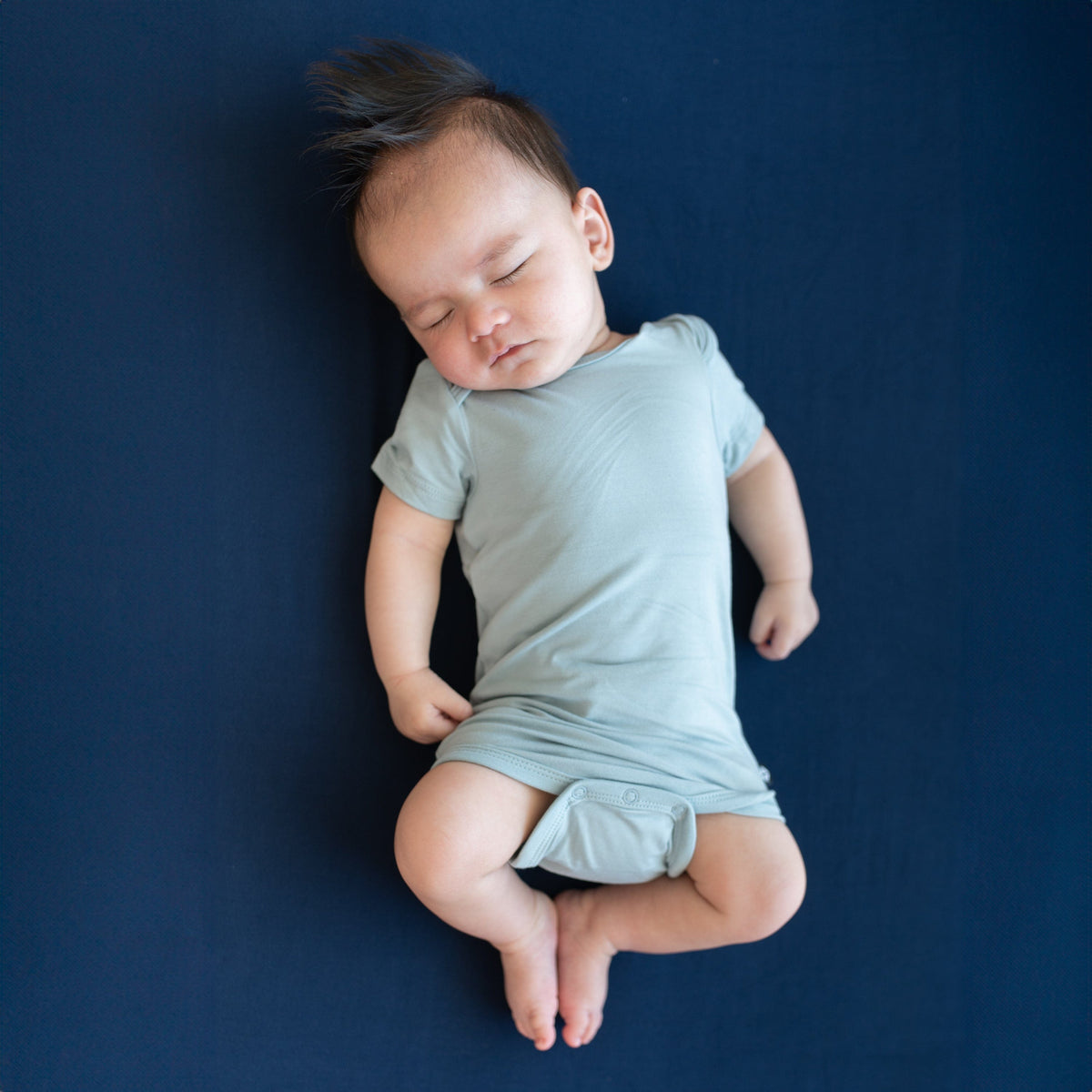 Sleeping baby laying on a Crib Sheet in Navy while wearing a Kyte Baby Bodysuit in Fog