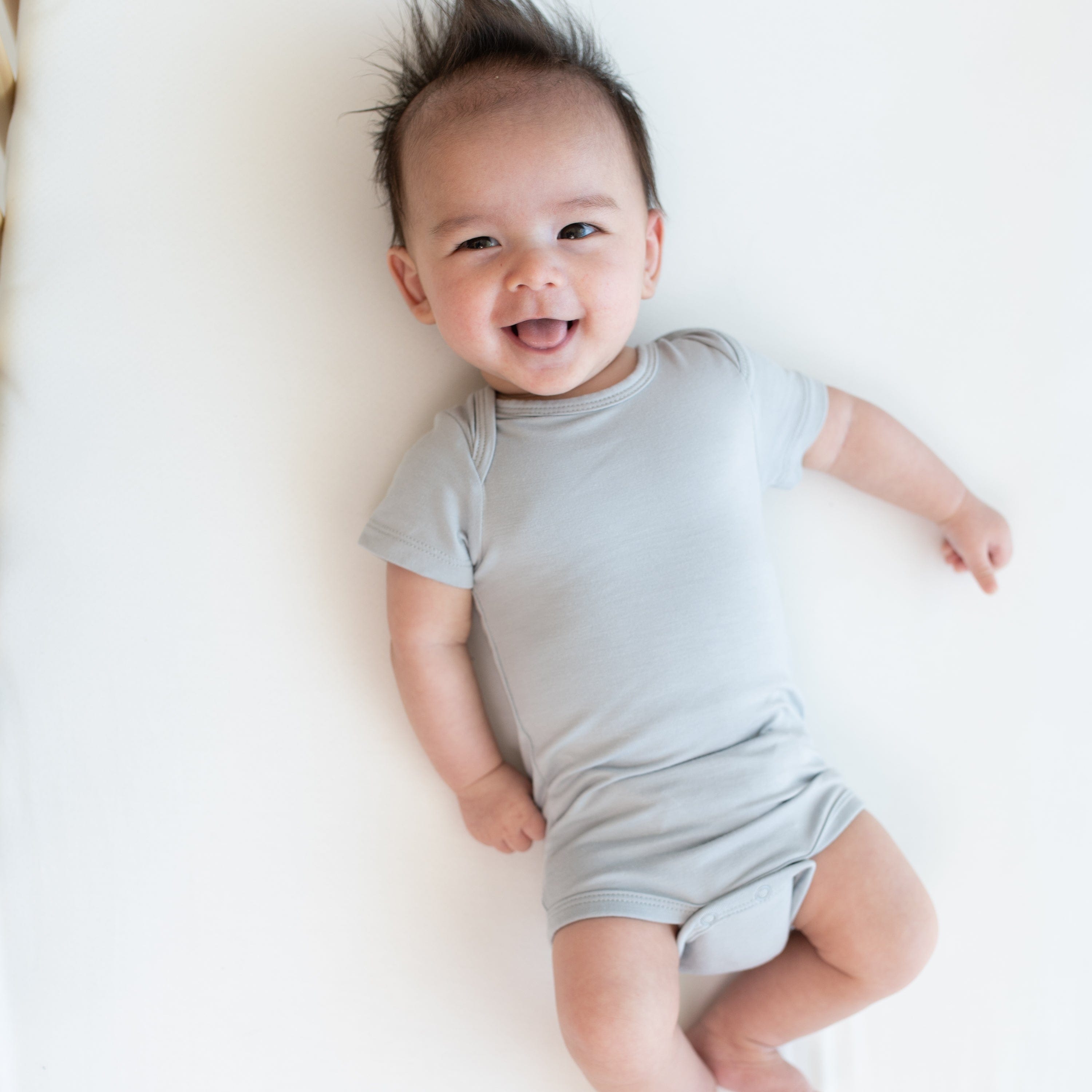 Baby laying in a crib wearing a Kyte Baby Bodysuit in Storm