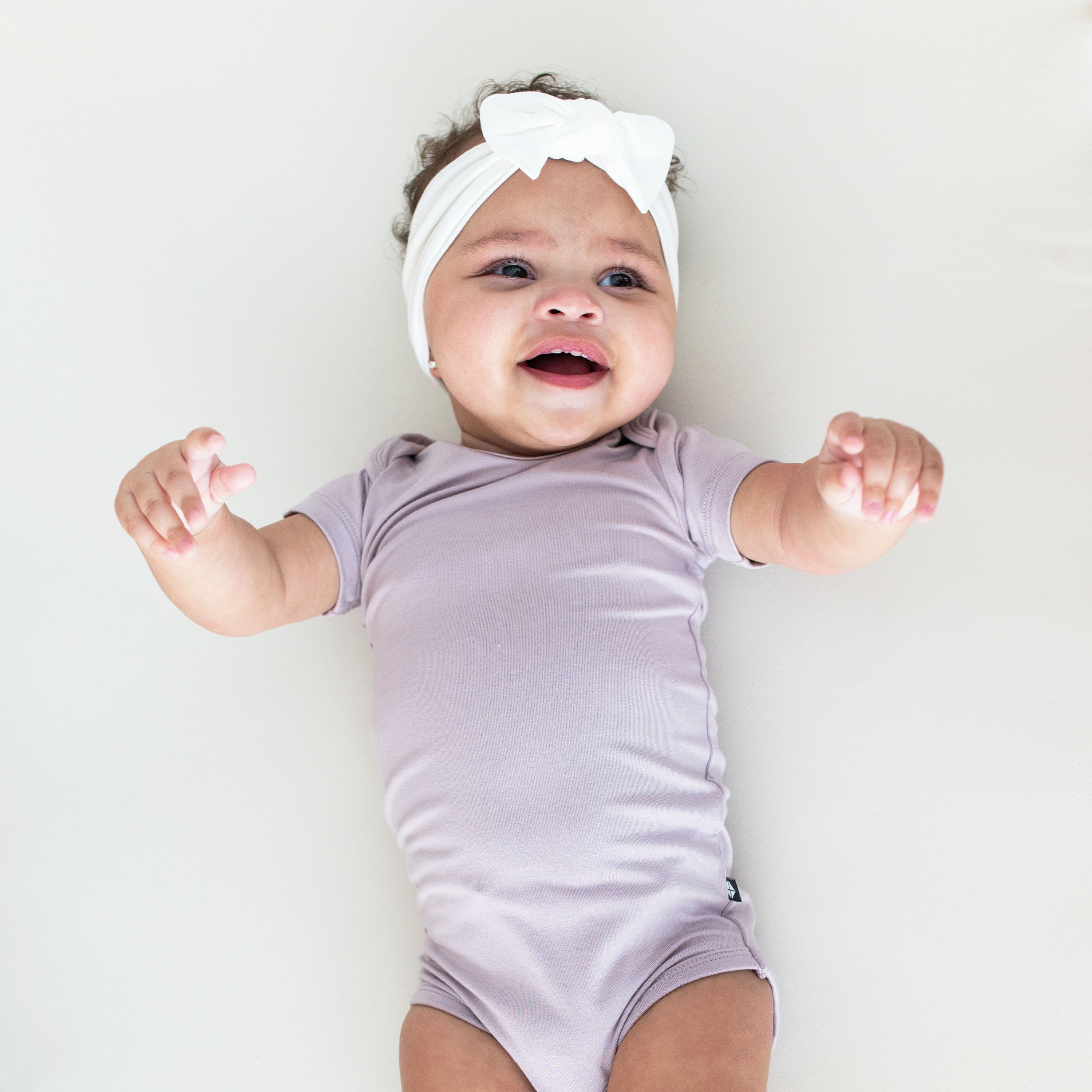 Infant wearing short sleeve Kyte Baby Bodysuit in Wisteria purple