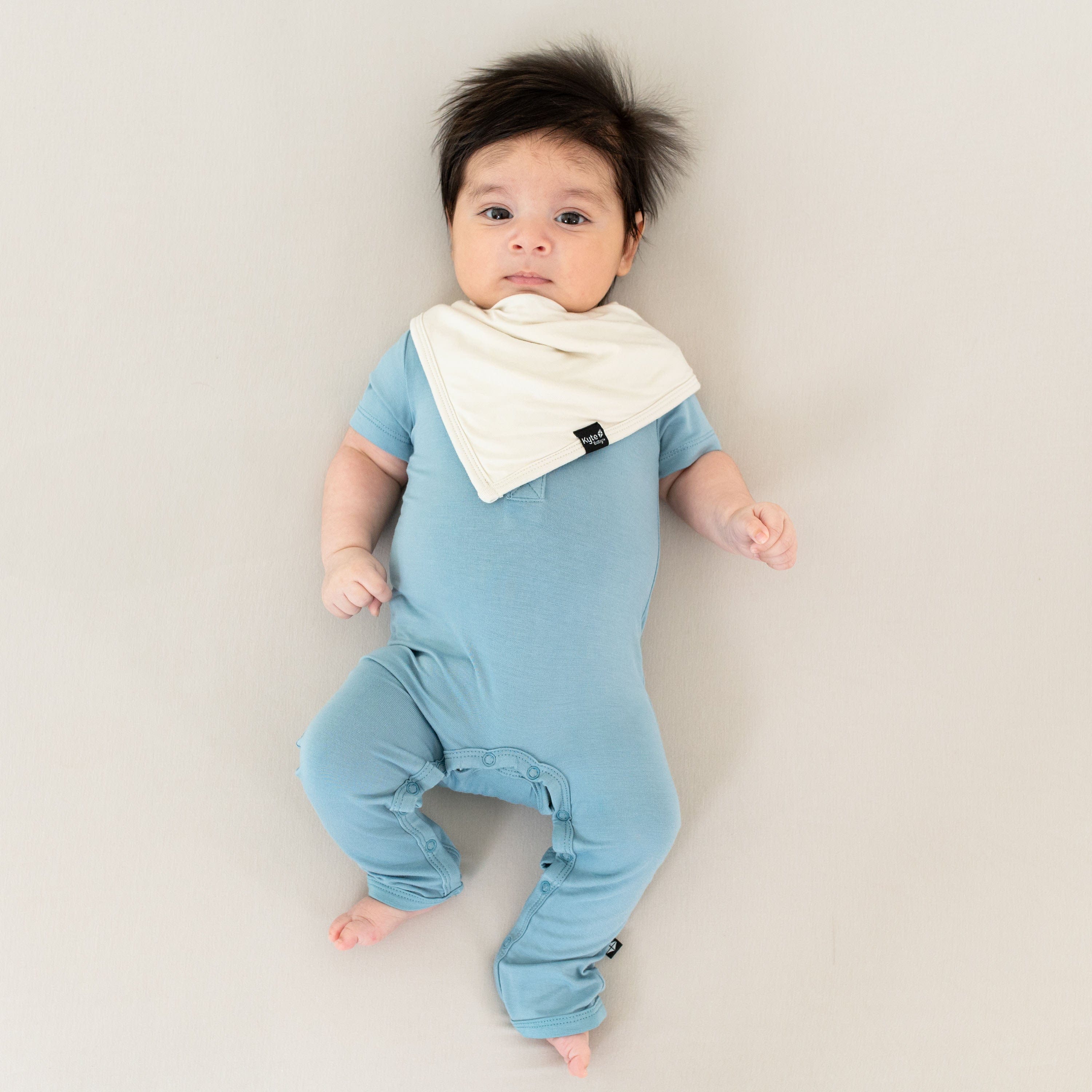 Baby wearing Kyte Baby Short Sleeve Snap Romper in Dusty Blue with bib