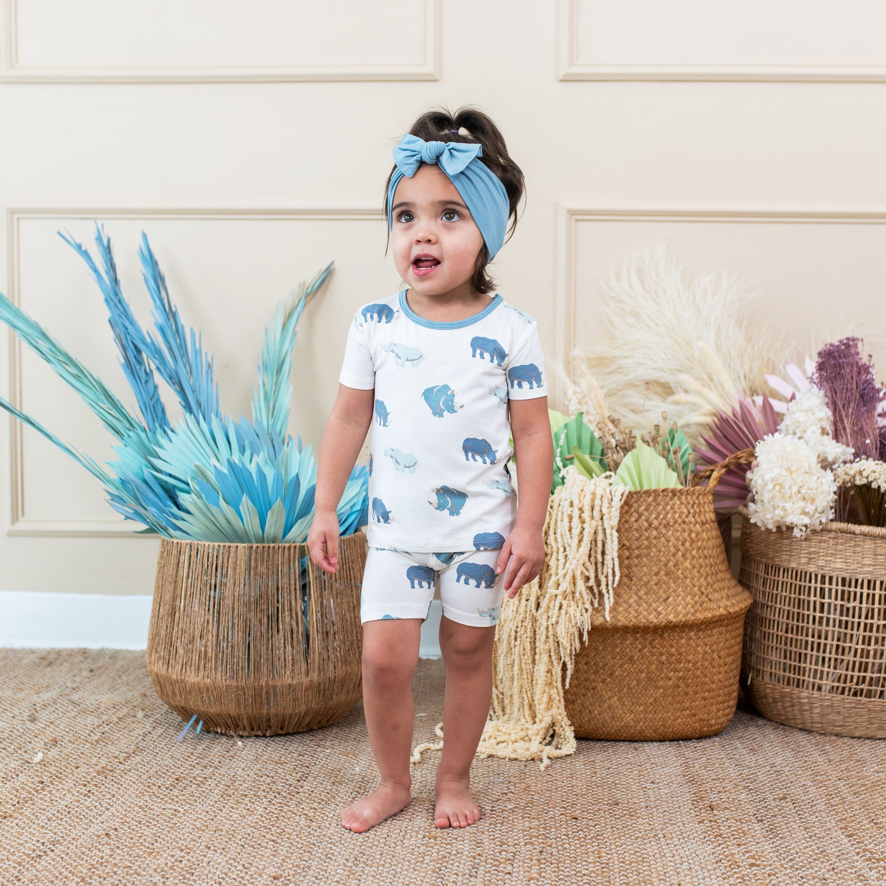 Child wearing Kyte Baby Short Sleeve Pajamas in Rhino with blue bow headband