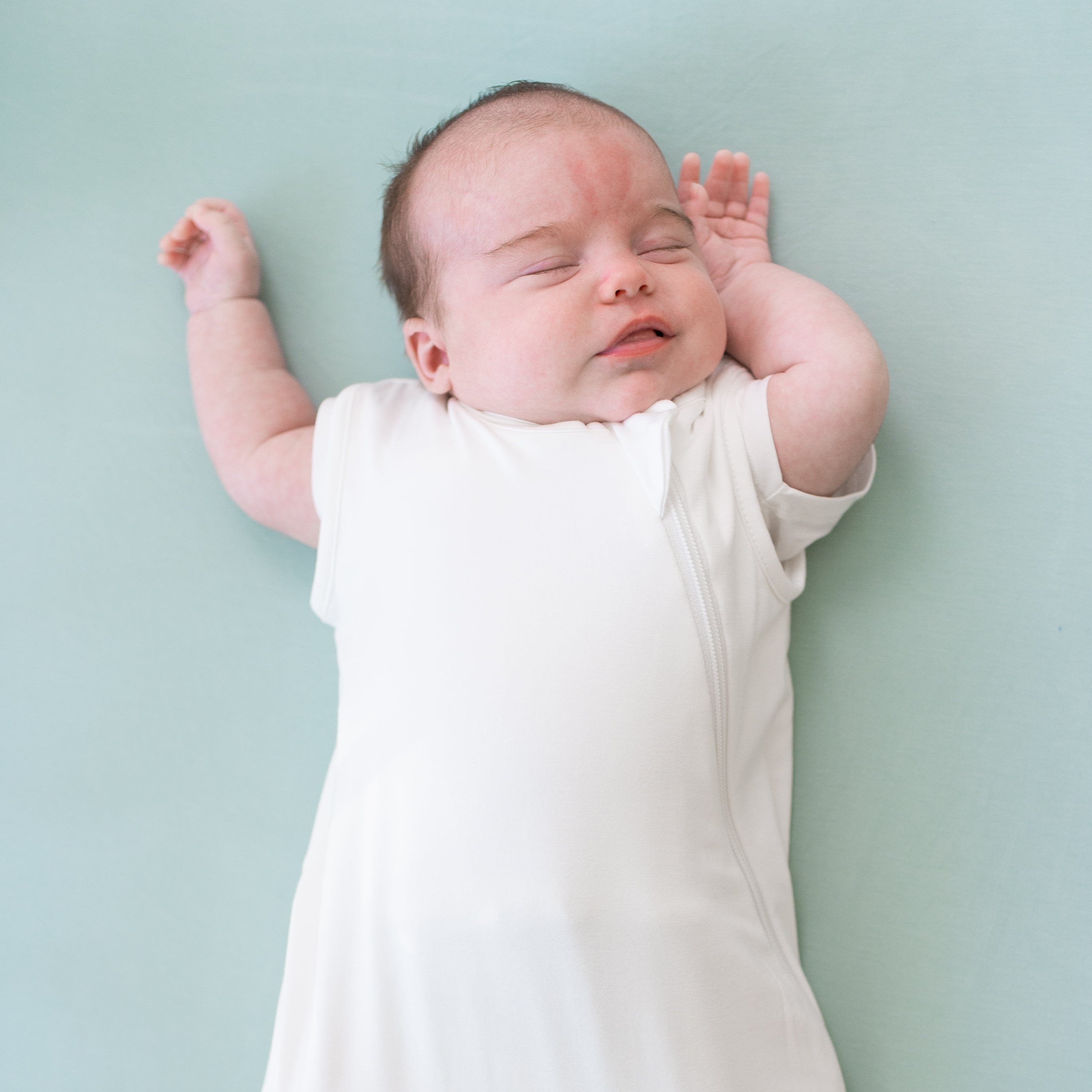 Sleeping baby laying on Crib Sheet in Sage wearing 0.5 Tog Sleep Bag in Cloud