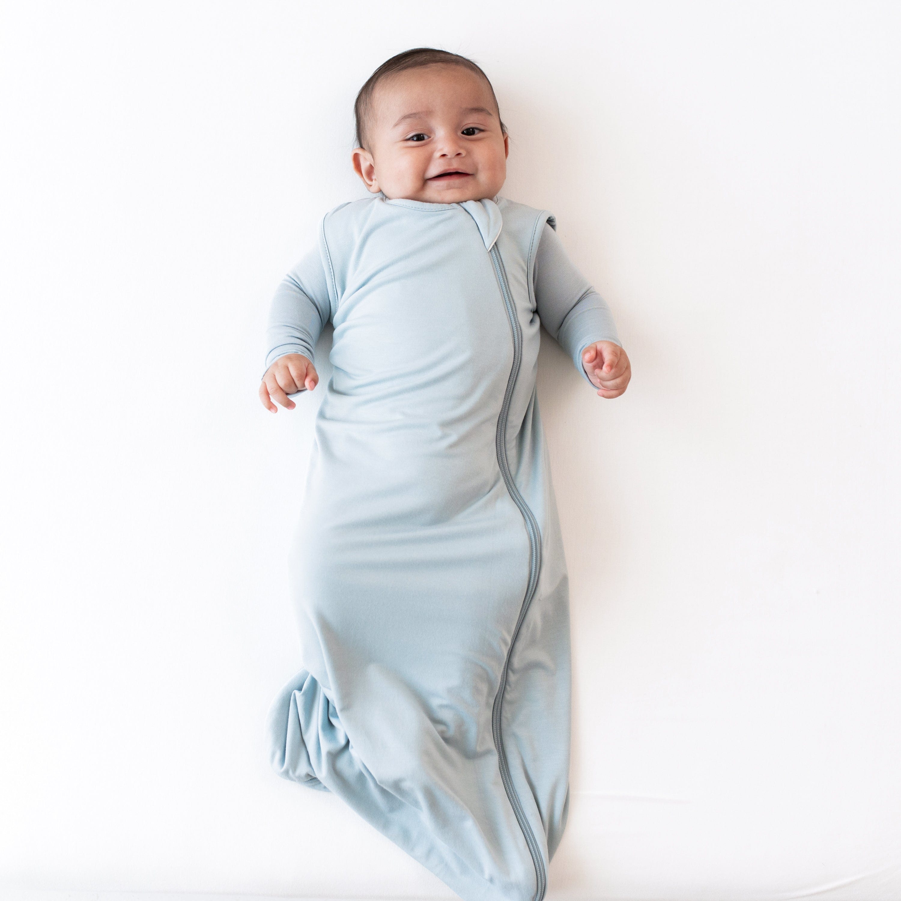 Smiling baby wearing the 0.5 Tog Sleep Bag in Fog with matching long sleeve bodysuit underneath