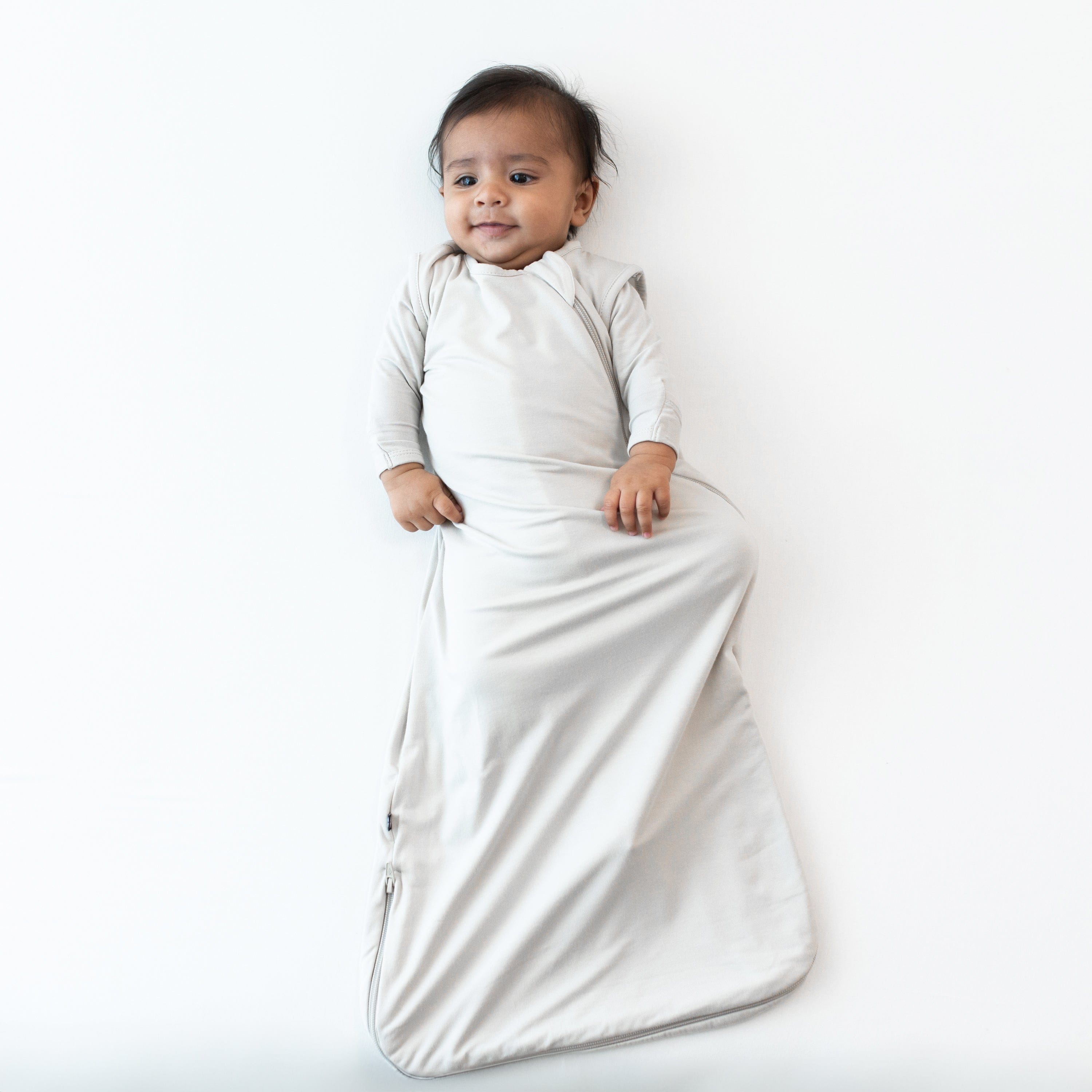 Infant modeling the 0.5 Tog Sleep Bag in Oat wearing an Oat long sleeve romper underneath