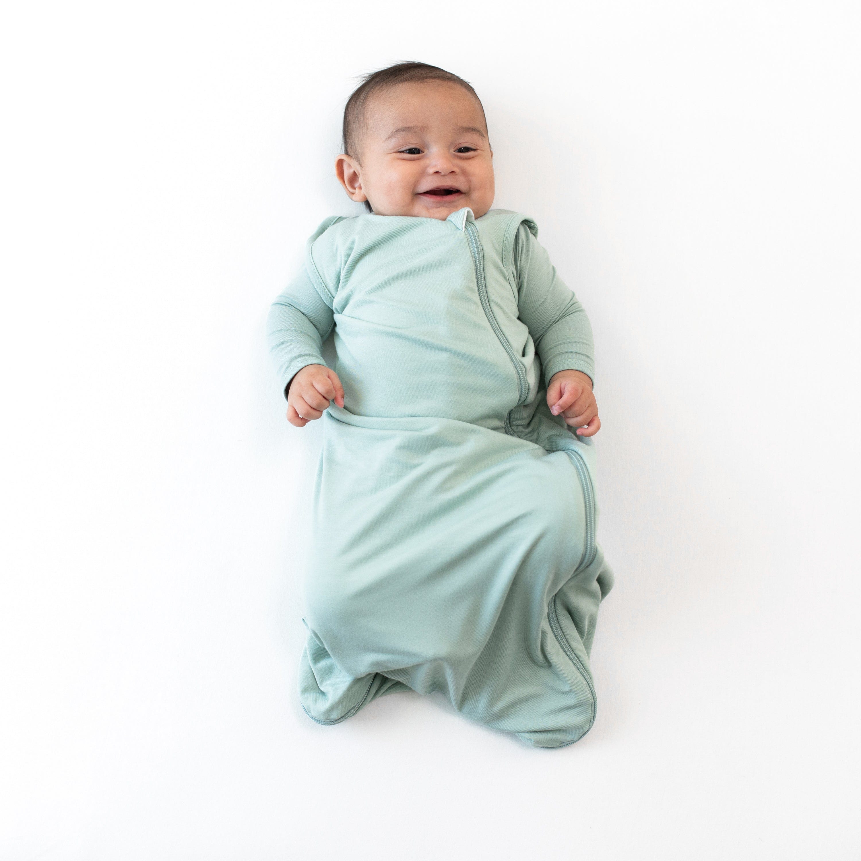 Smiling infant wearing the 0.5 Tog Sleep Bag in Sage with a Sage long sleeve romper underneath