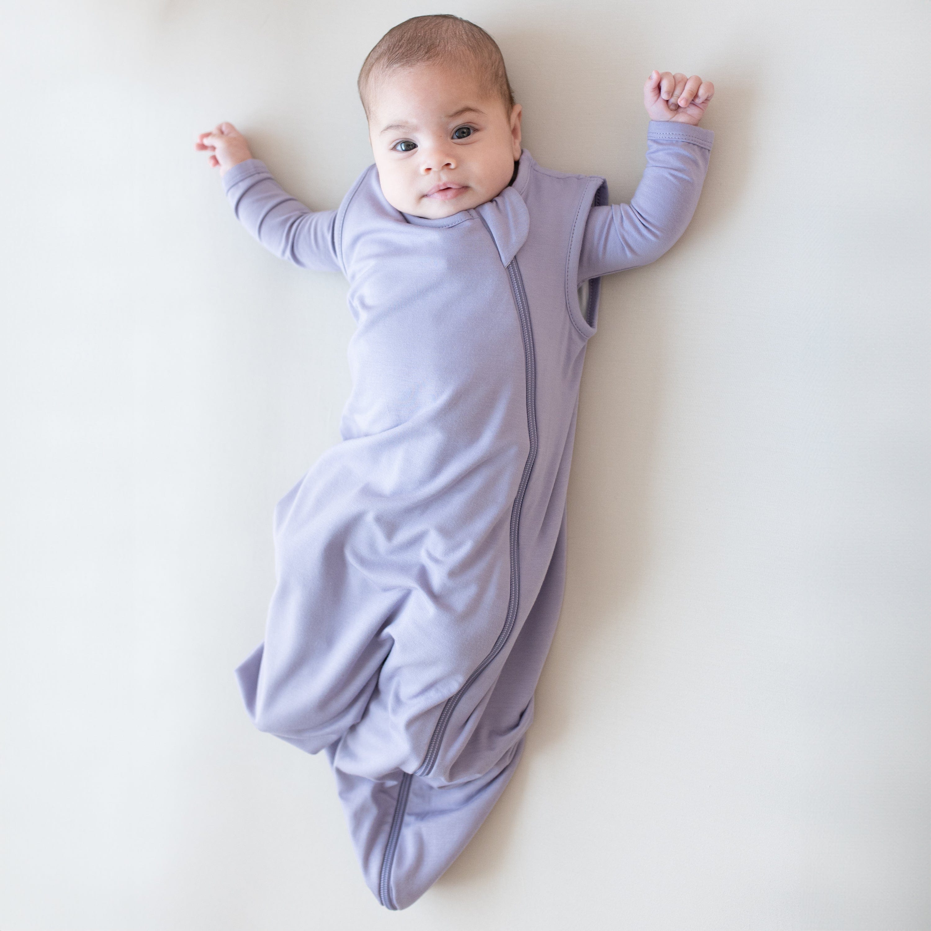 Baby modeling the 0.5 Tog Sleep Bag in Taro with a Taro long sleeve romper underneath