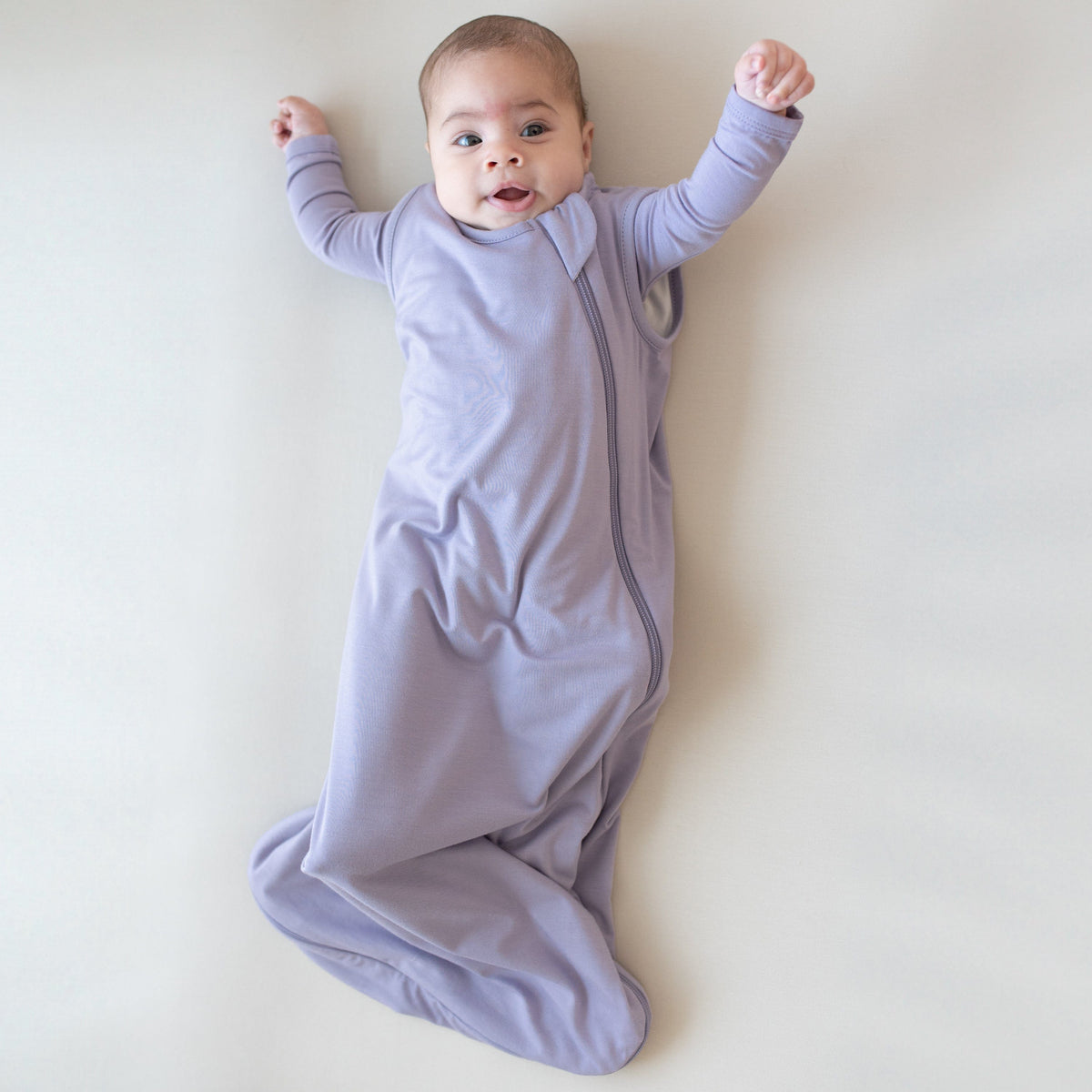 Infant modeling the 0.5 Tog Sleep Bag in Taro with a long sleeve romper in Taro underneath