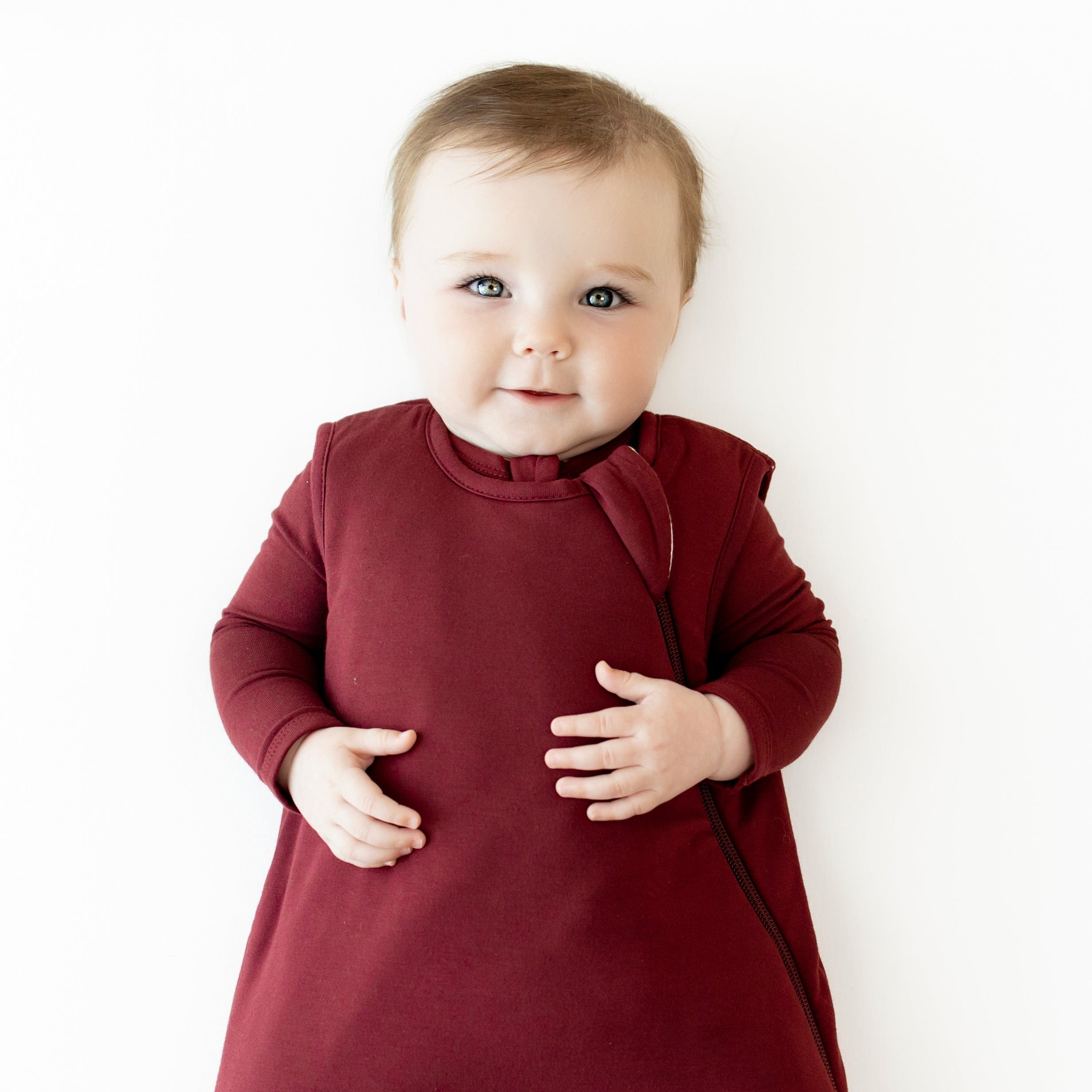 Close up of baby wearing the Sleep Bag in Burgundy 1.0 with matching long sleeve romper on underneath