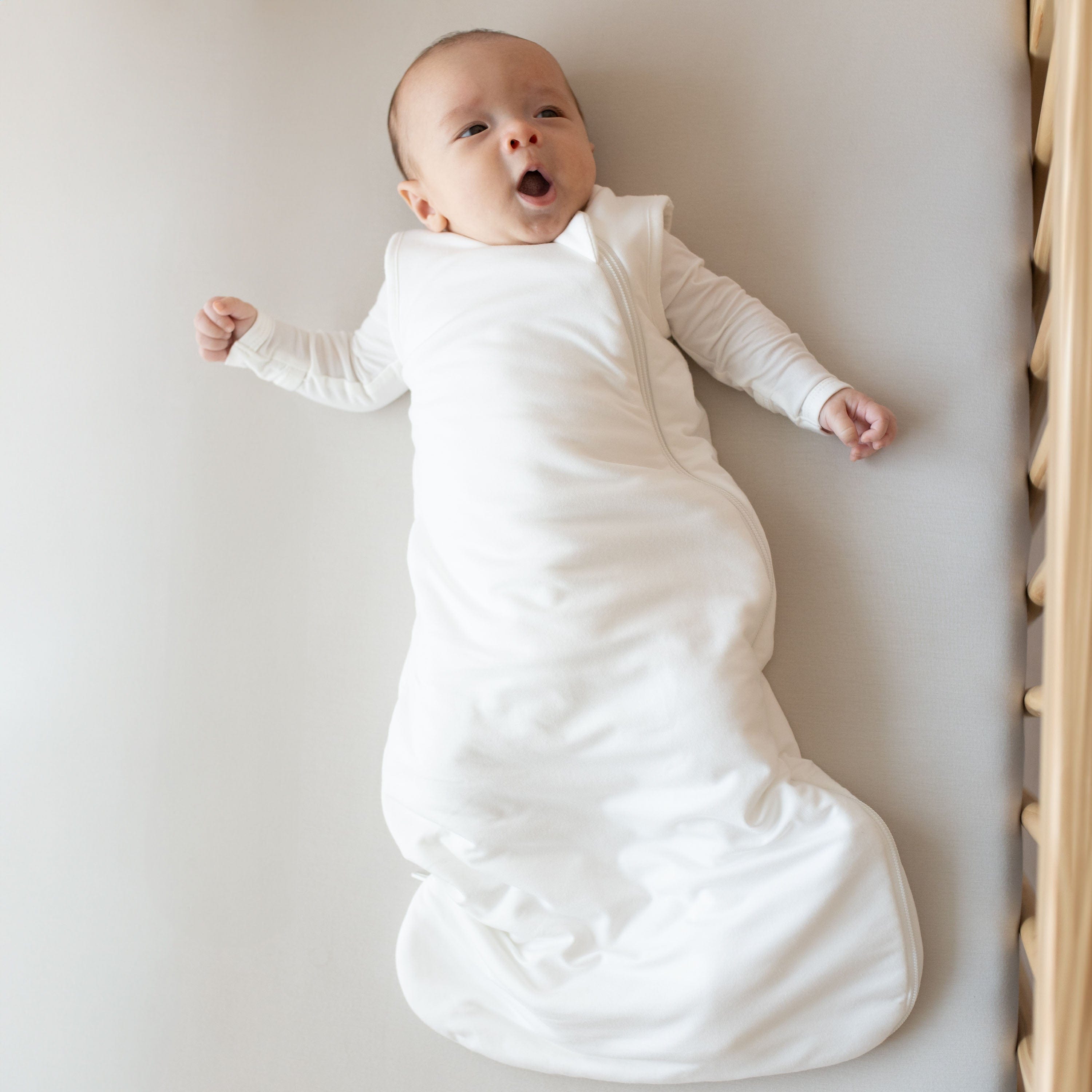 Yawning baby wearing the Sleep Bag in Cloud 1.0 with a Cloud long sleeve romper underneath