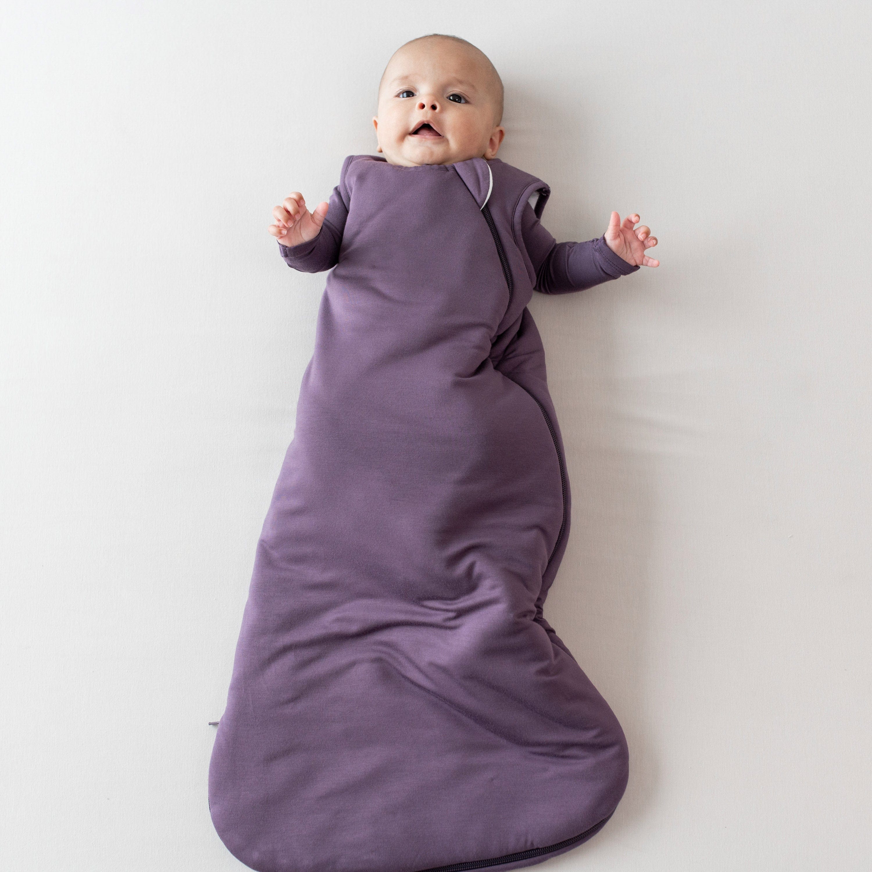 Baby wearing the 1.0 Sleep Bag in Currant with a Currant long sleeve romper underneath