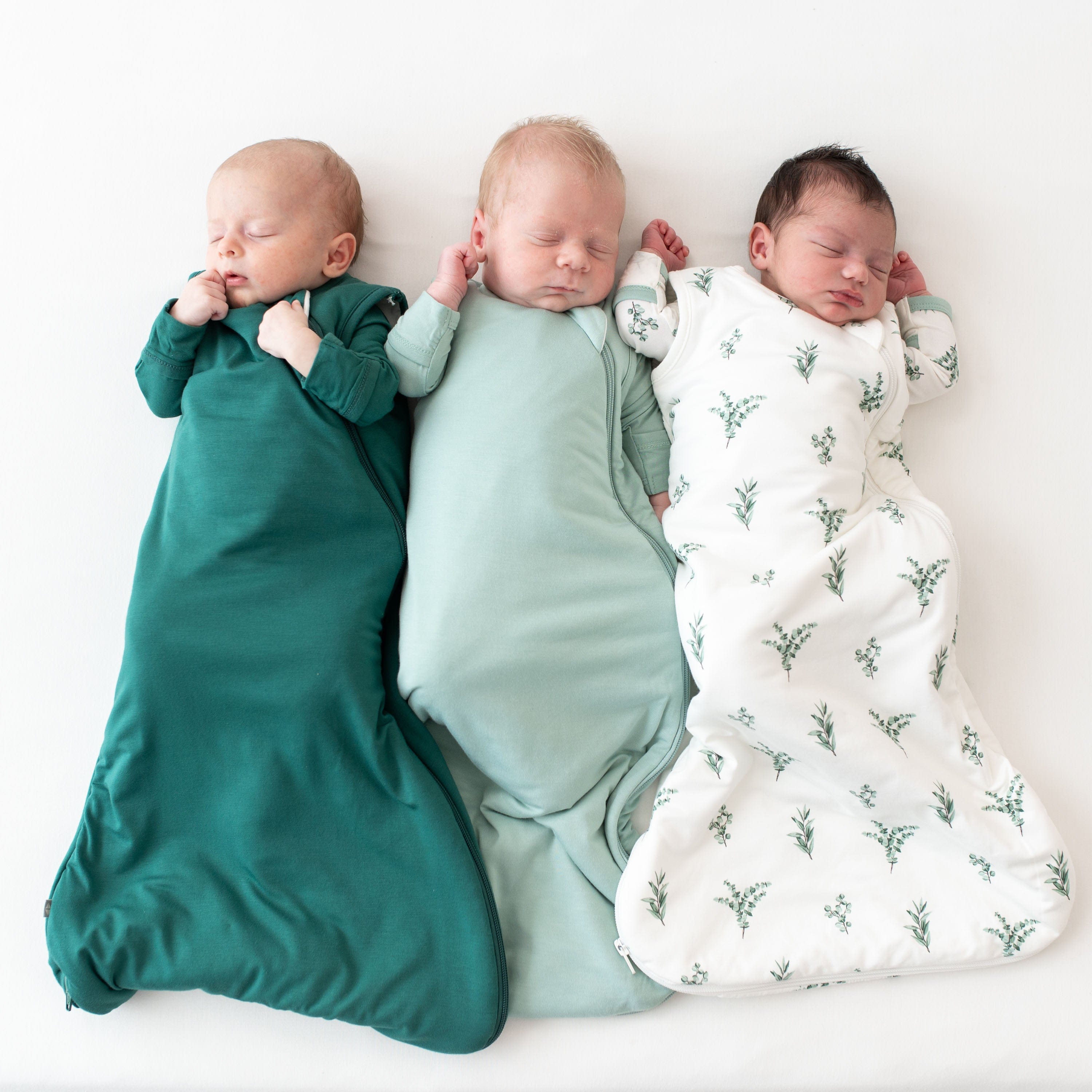 Three sleeping babies wearing the 1.0 Sleep Bags in Emerald, Sage and the print Eucalyptus