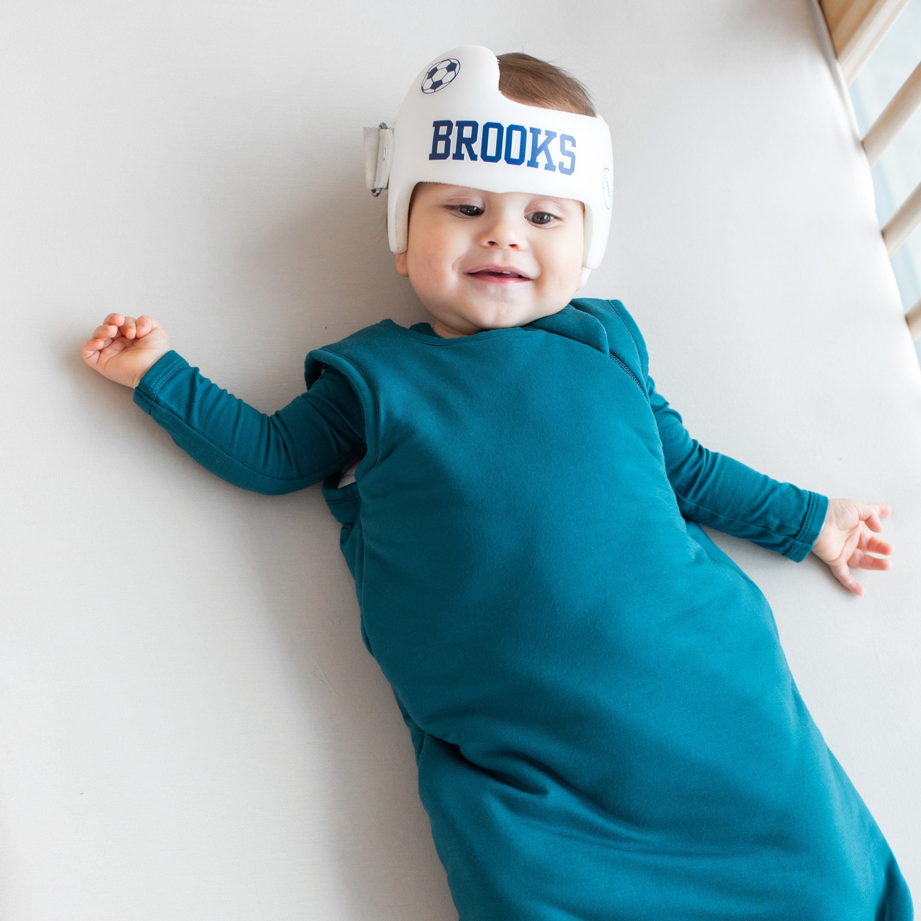 Smiling infant model wearing a 1.0 Sleep Bag in Loch with a Loch long sleeve romper underneath