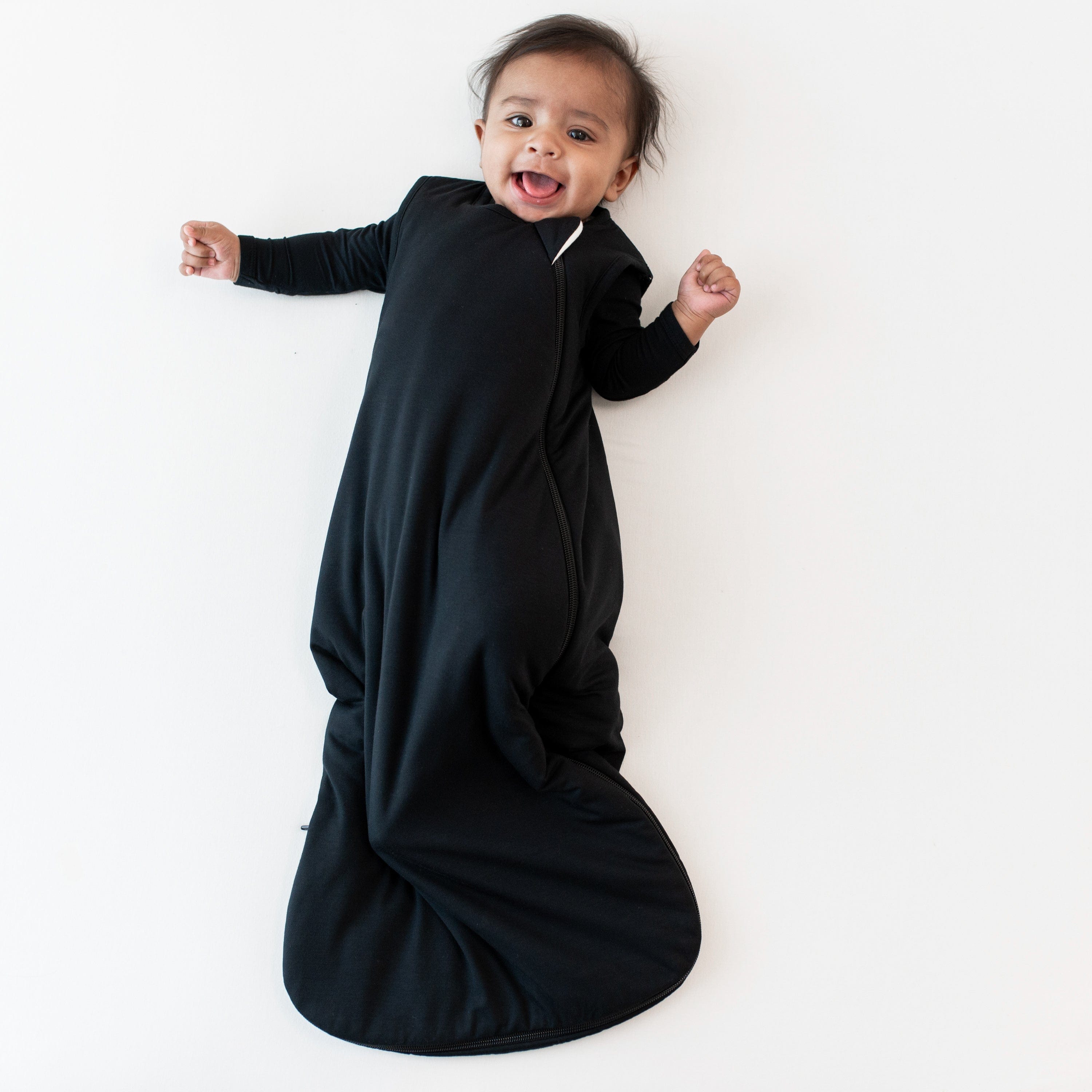 Smiling infant wearing Kyte Baby Sleep Bag in Midnight 1.0 with a Midnight long sleeve romper underneath