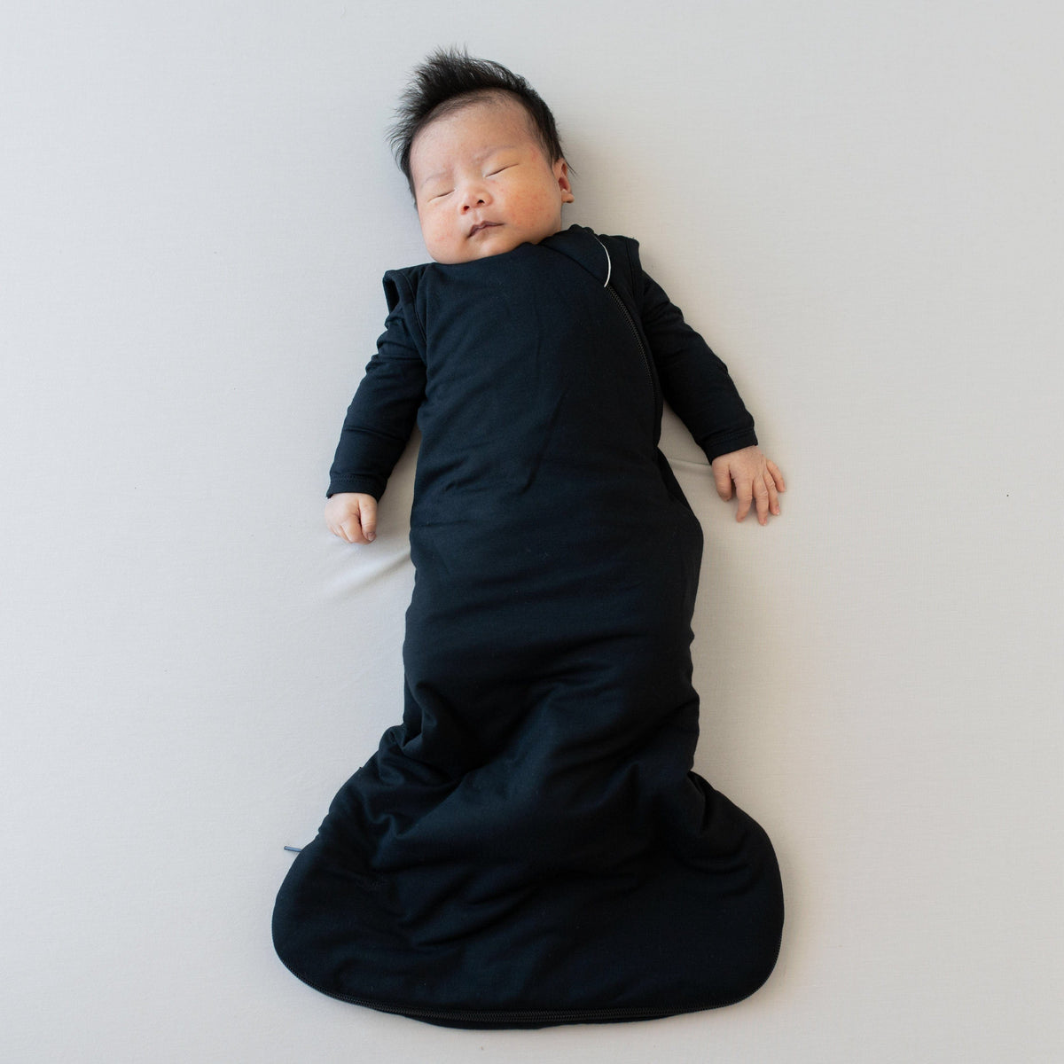 Sleeping infant in Kyte Baby Sleep Bag in Midnight 1.0 and a matching long sleeve bodysuit underneath