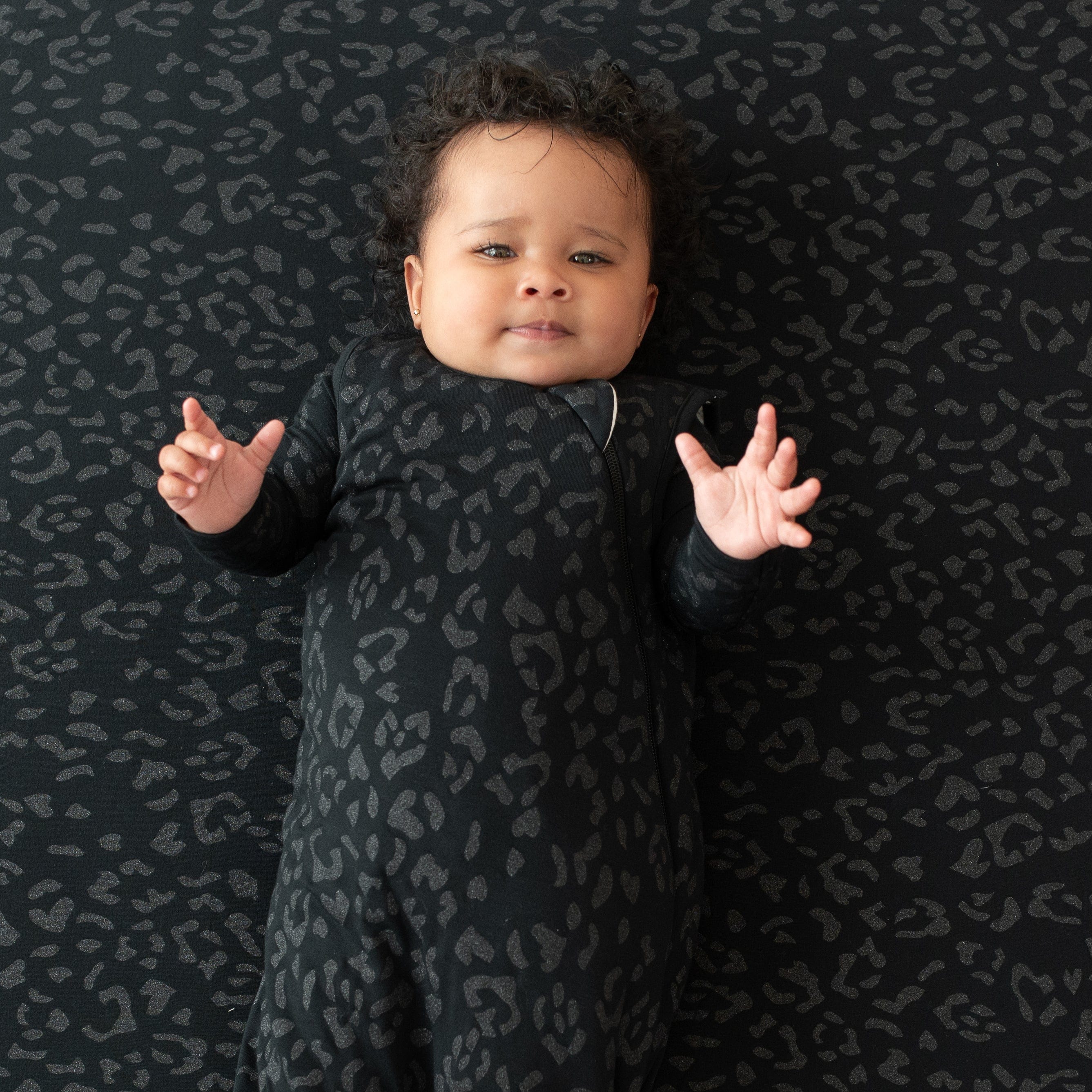 Infant modeling the Sleep Bag in Midnight Leopard 1.0 laying on top of a Midnight Leopard blanket