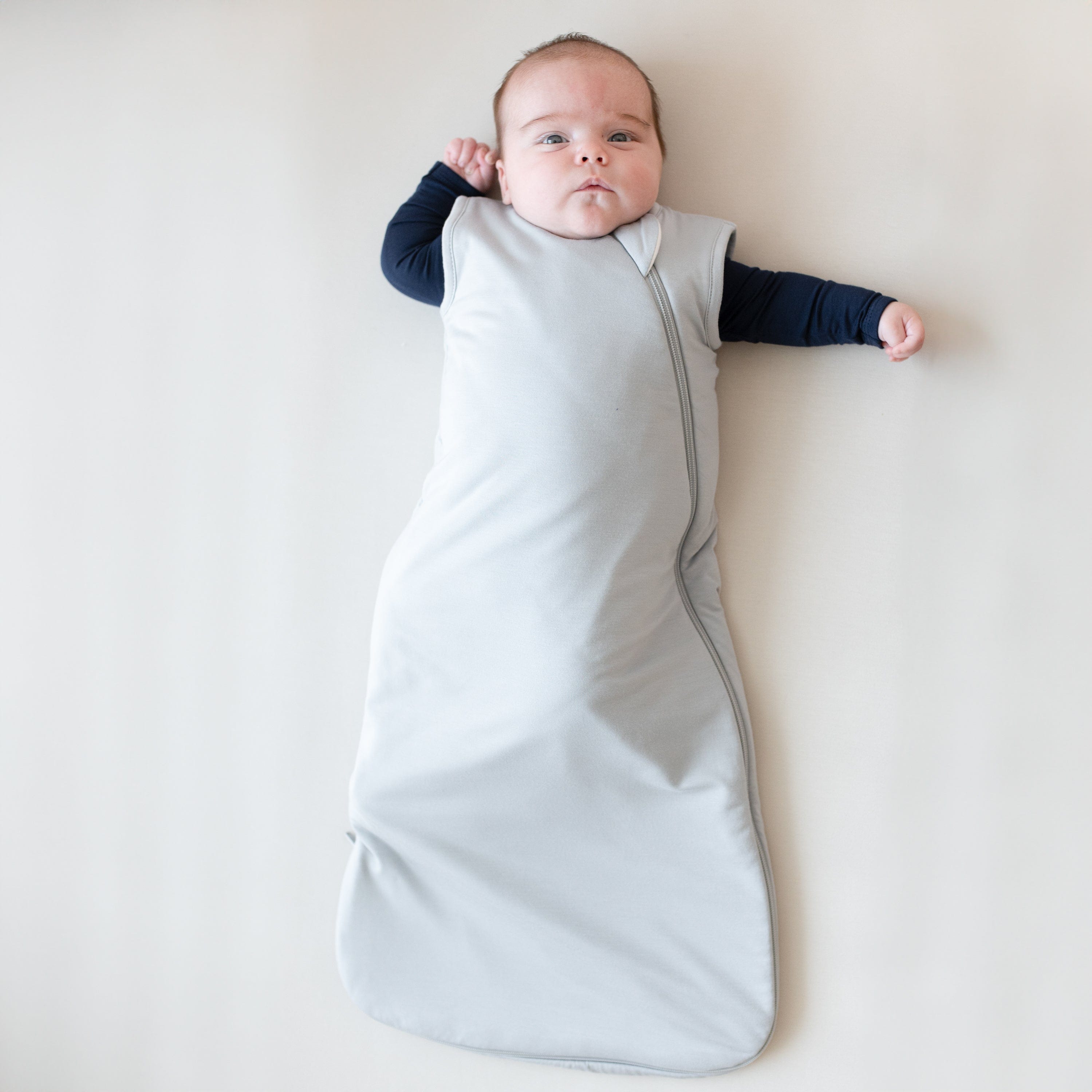 Infant model wearing Kyte Baby Sleep Bag in Storm 1.0 with long sleeve Bodysuit in Navy underneath