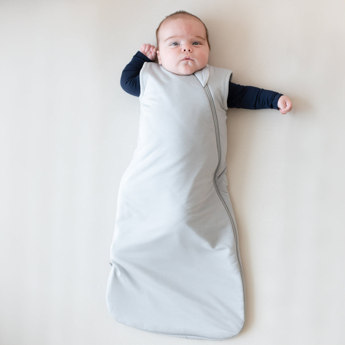 Infant model wearing Kyte Baby Sleep Bag in Storm 1.0 with long sleeve Bodysuit in Navy underneath