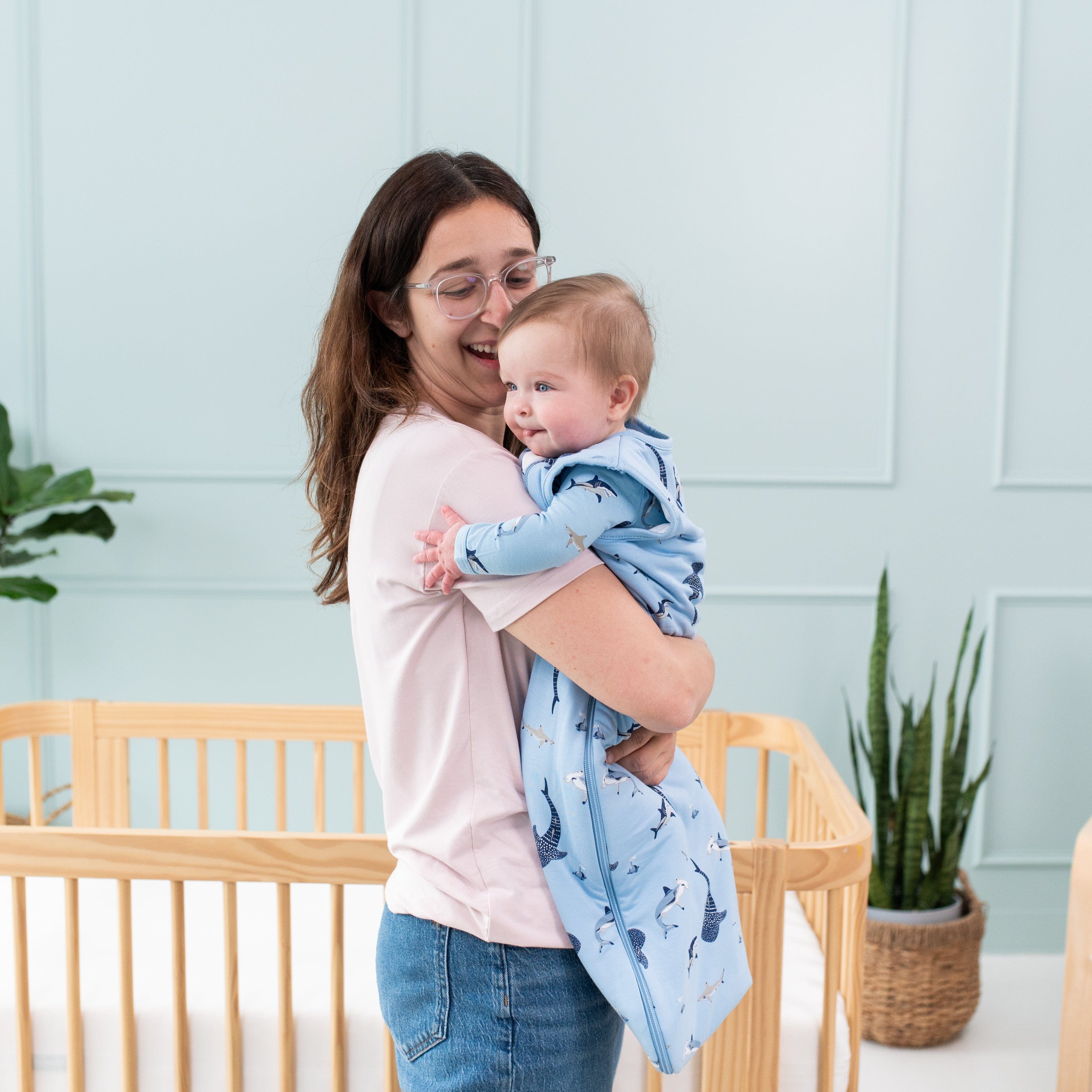 Mom holding infant wearing Kyte Baby bamboo Sleep Bag in Stream Shark 1.0