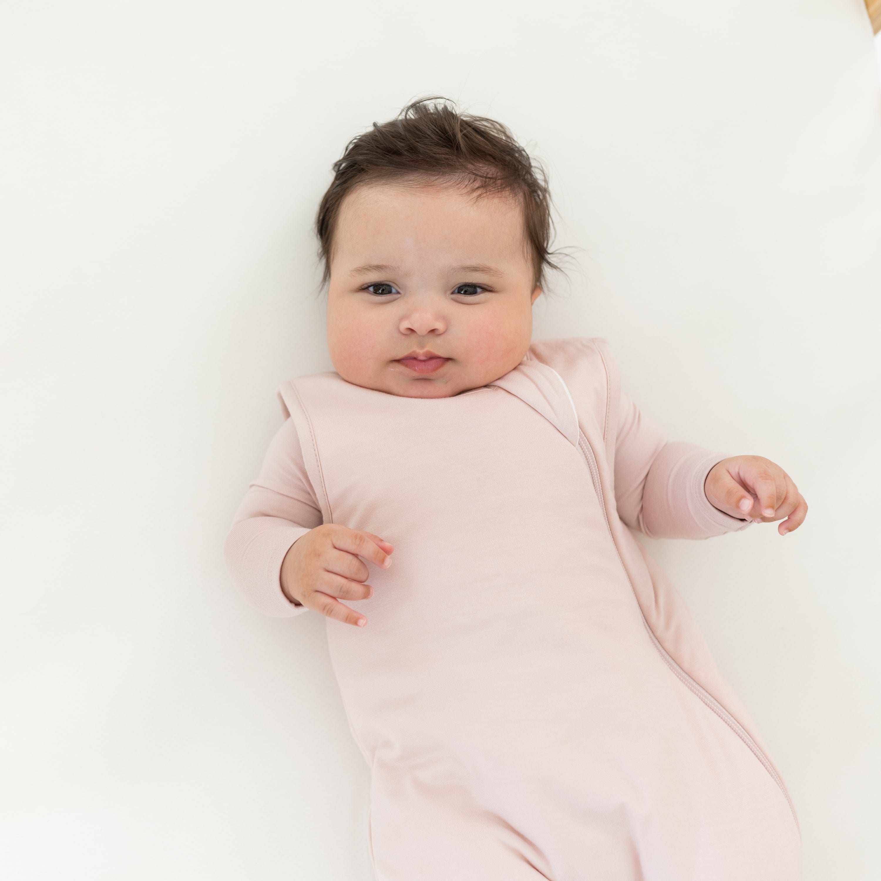 Infant wearing the Sleep Bag in Blush 2.5 with a matching long sleeve bodysuit underneath