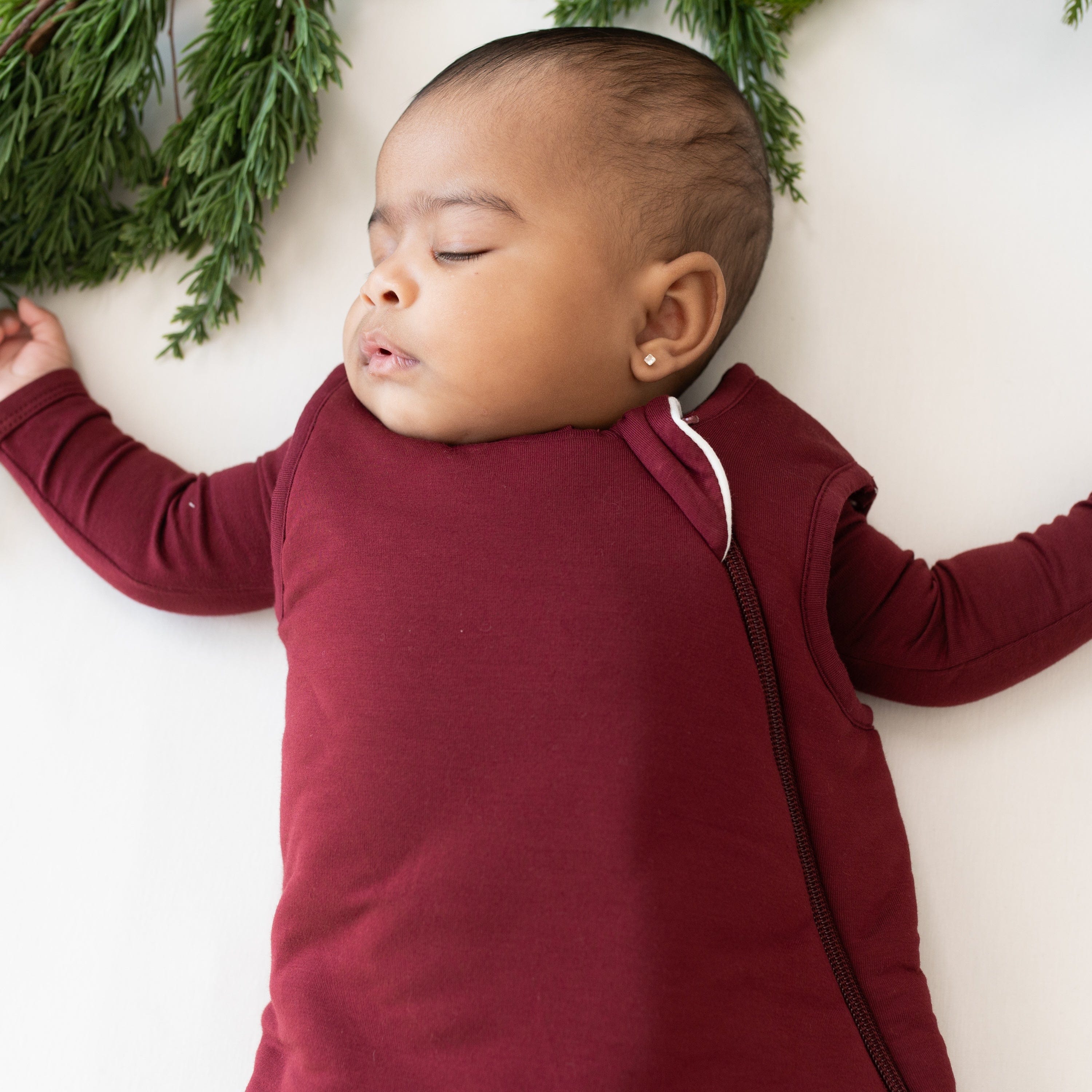 Sleeping infant wearing the Sleep Bag in Burgundy 2.5 with matching long sleeve romper on underneath