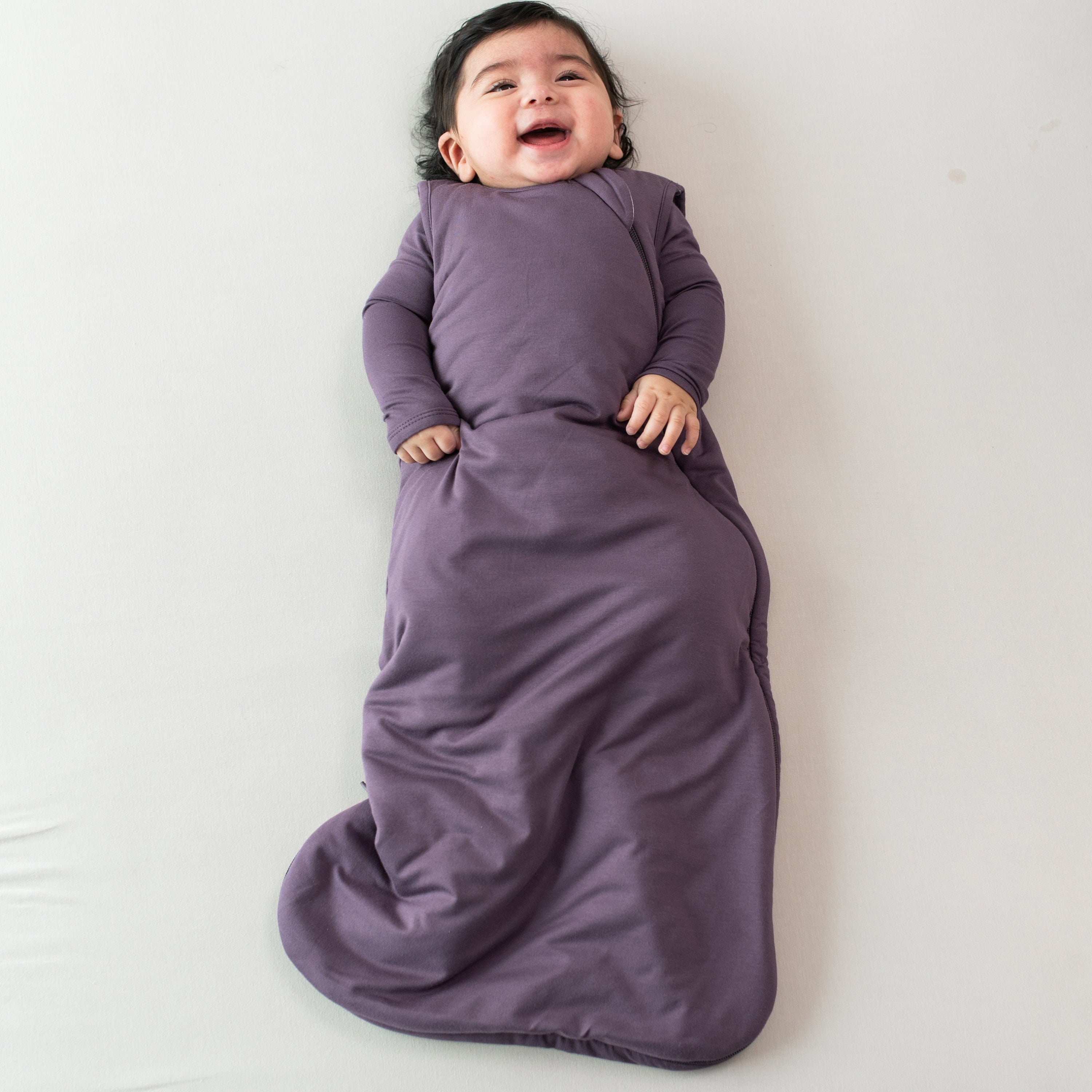 Smiling infant wearing the Sleep Bag in Currant 2.5 with a Currant long sleeve romper underneath