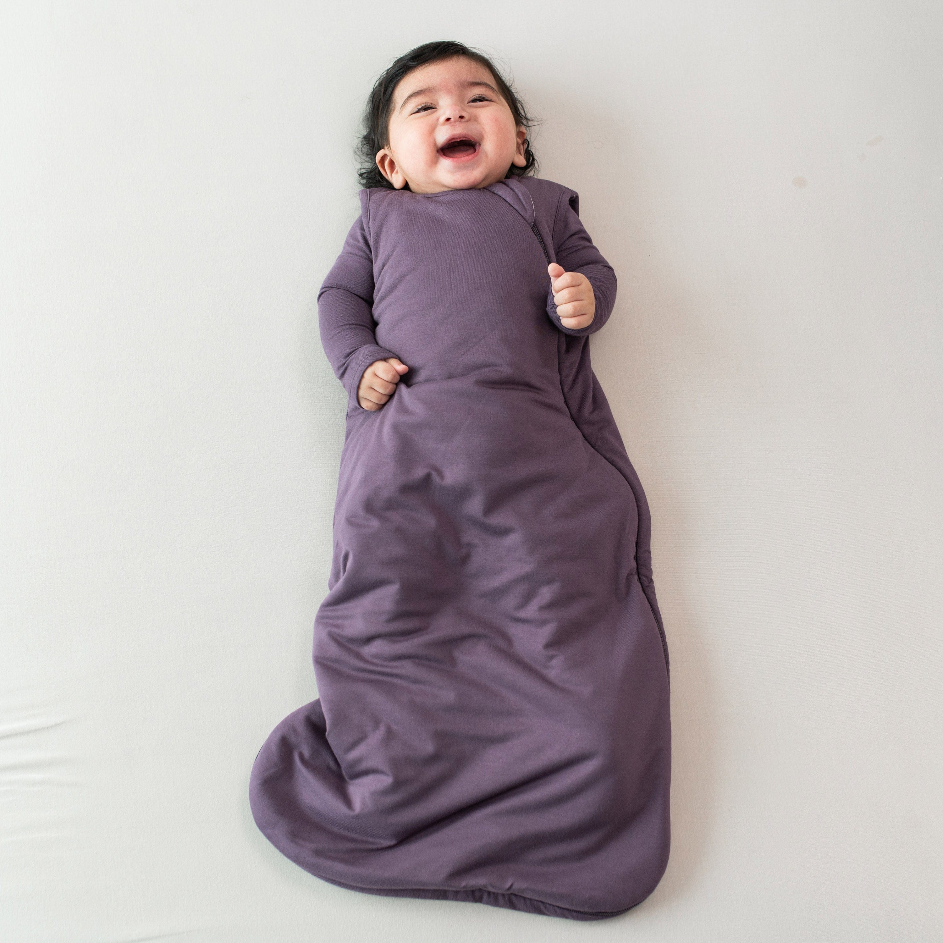 Smiling infant wearing the Sleep Bag in Currant 2.5 with a Currant long sleeve romper underneath