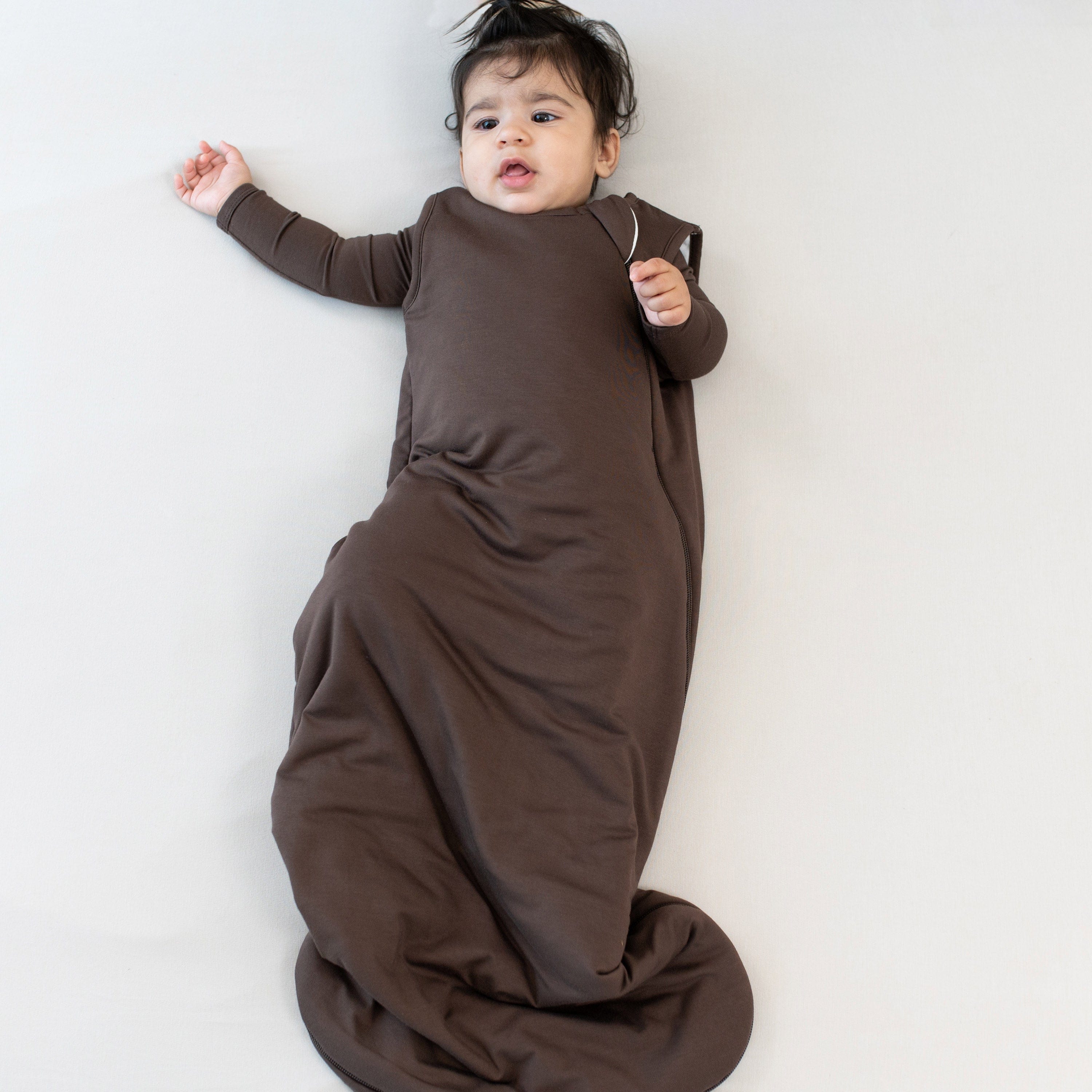 Infant laying down wearing the Sleep Bag in Espresso 2.5 with matching long sleeve romper on underneath