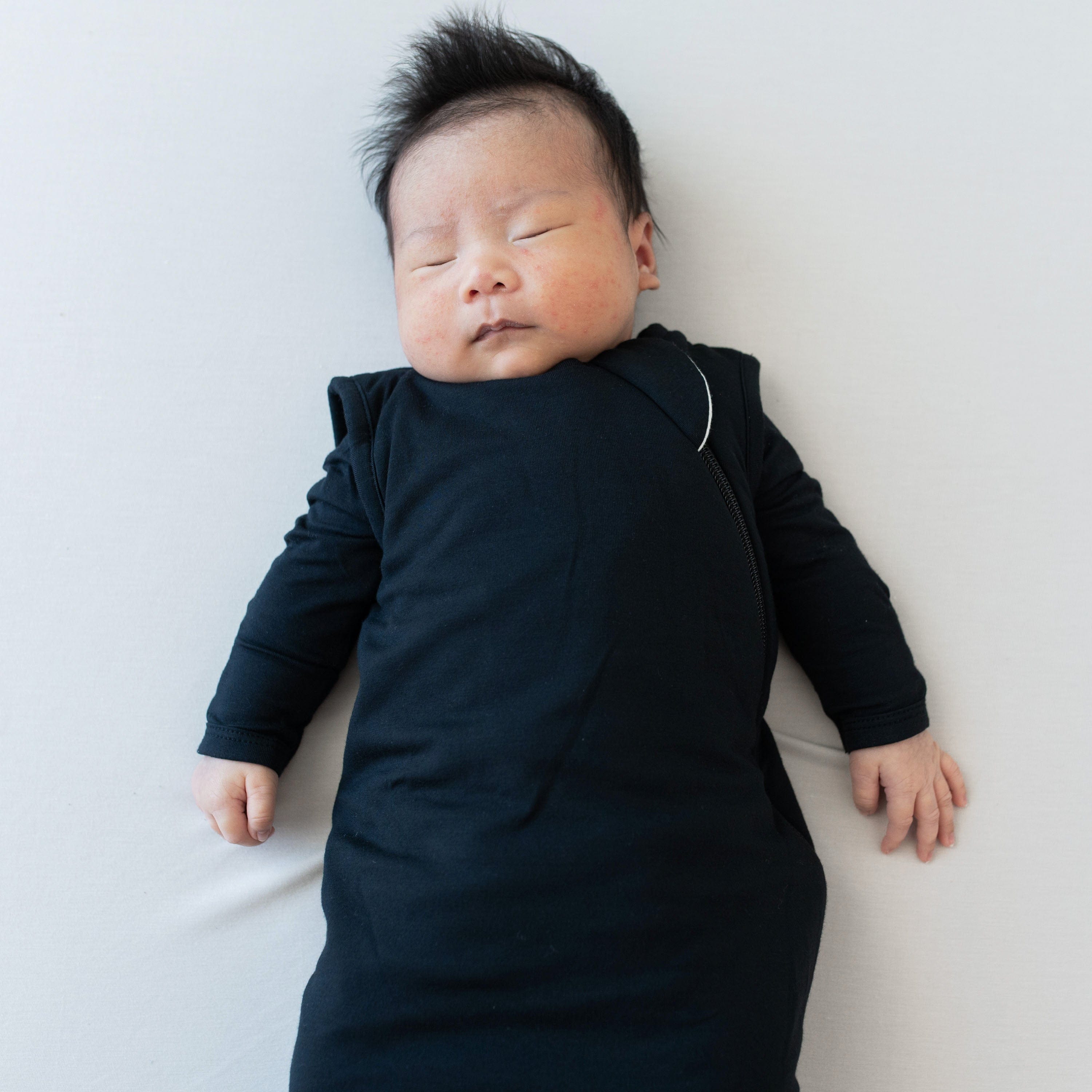 Sleeping baby wearing the Sleep Bag in Midnight 2.5 with a Midnight long sleeve romper underneath