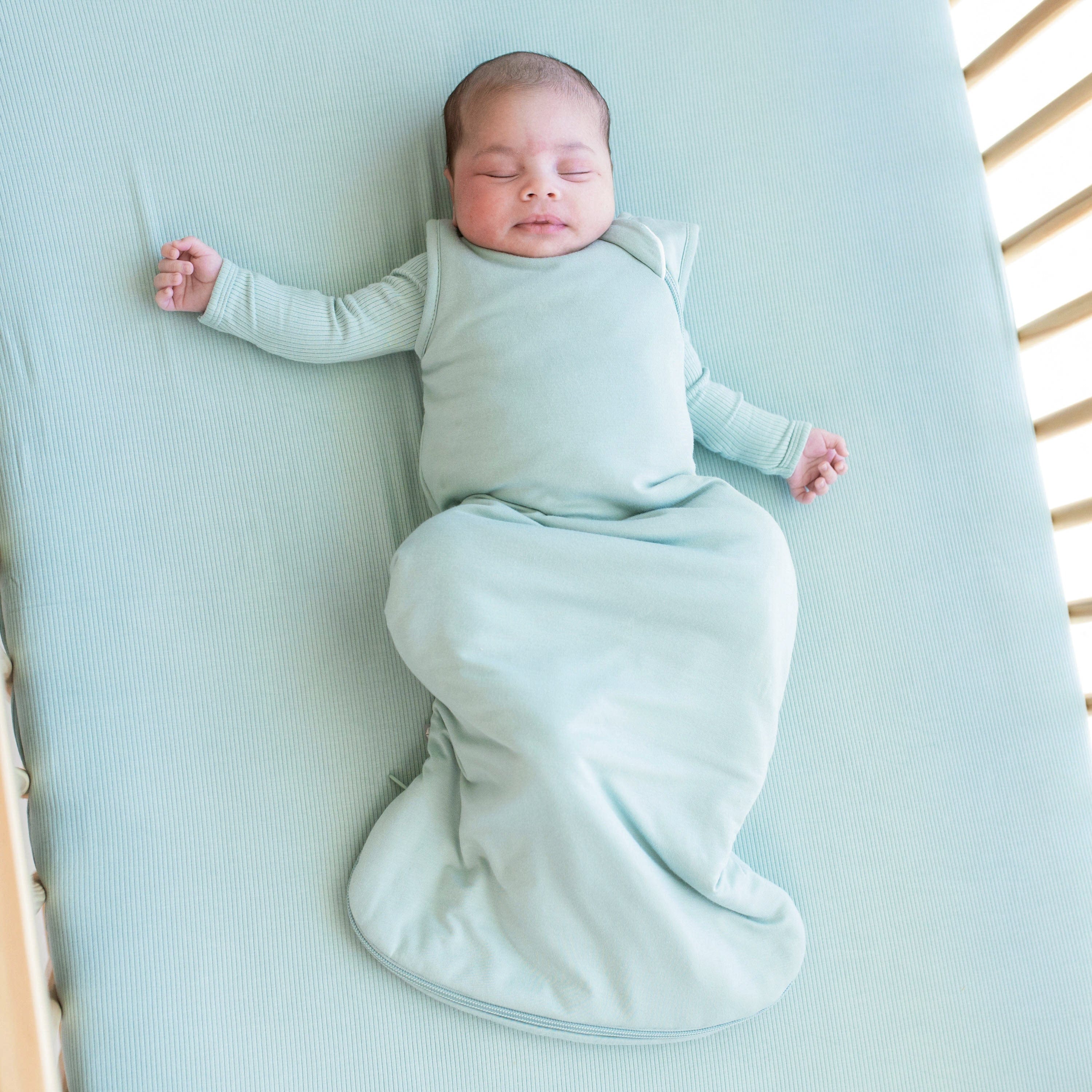 Infant sleeping in a crib and wearing a Sleep Bag in Sage 2.5 with a long sleeve Sage romper underneath