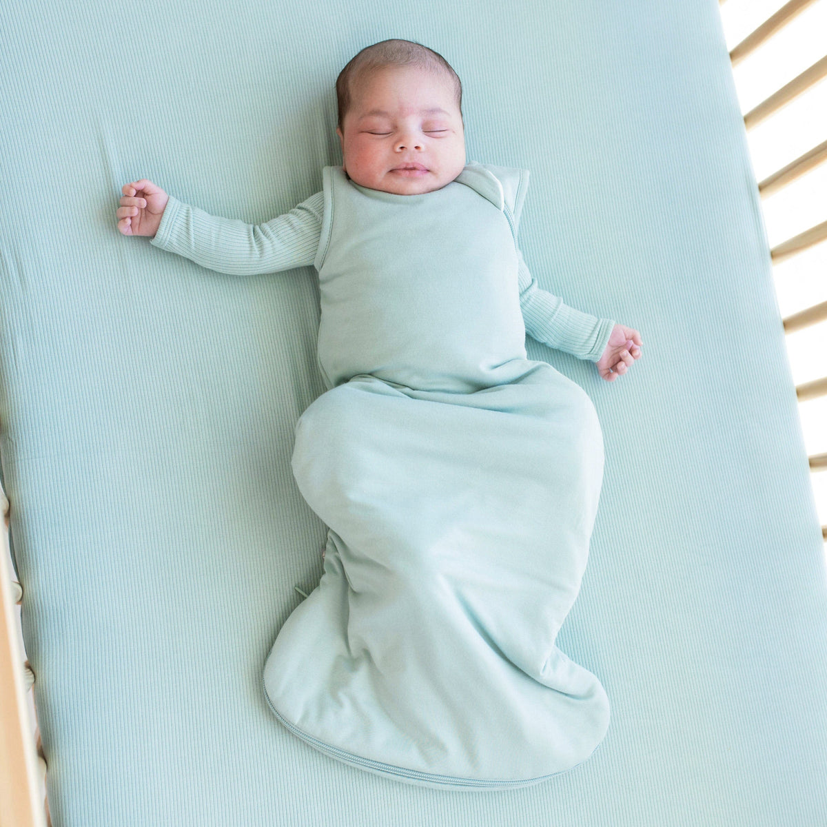 Infant sleeping in a crib and wearing a Sleep Bag in Sage 2.5 with a long sleeve Sage romper underneath