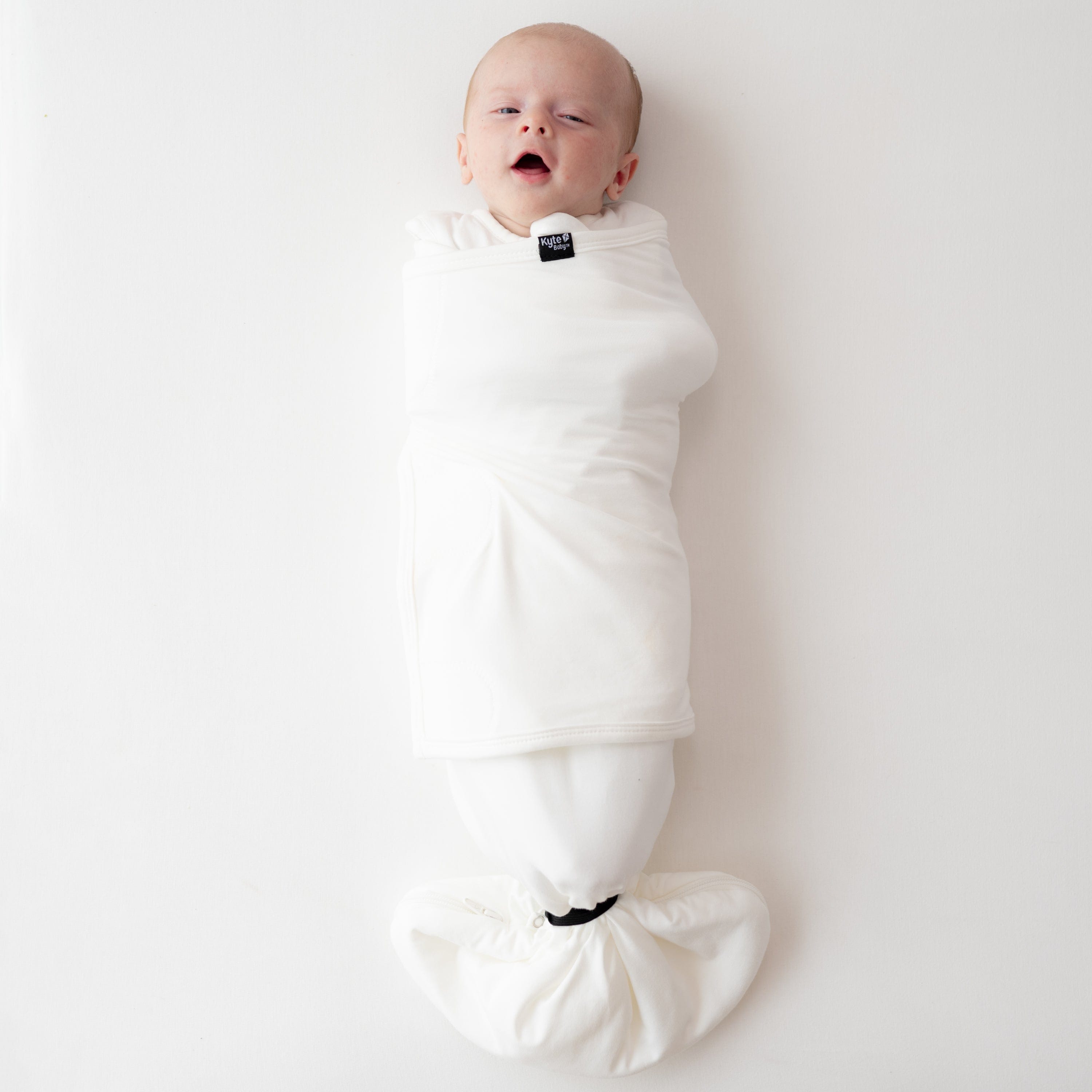 Baby wearing Kyte Baby Sleep Bag Swaddler in Cloud with elastic band