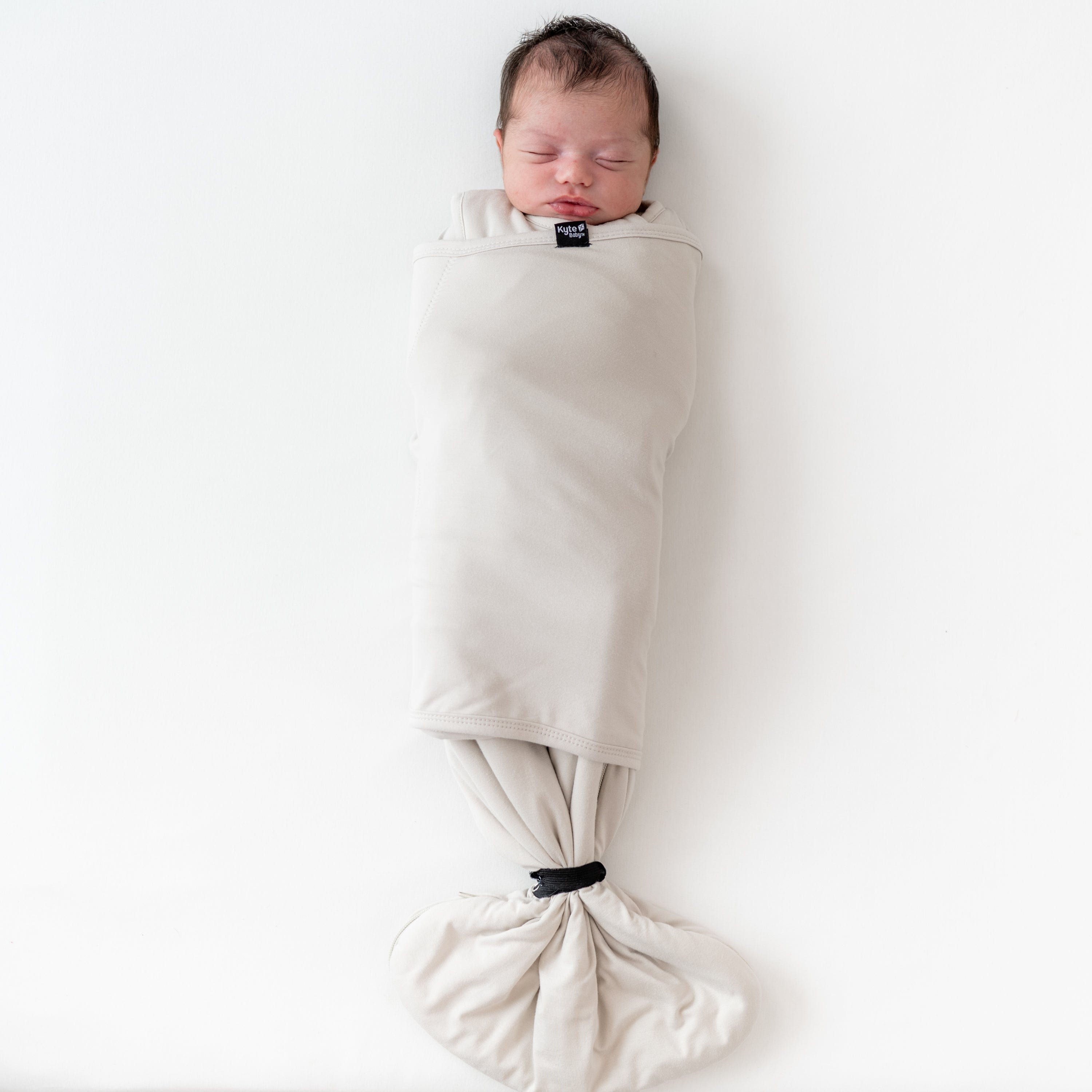 Baby wearing Kyte Baby Sleep Bag Swaddler in Oat with elastic band
