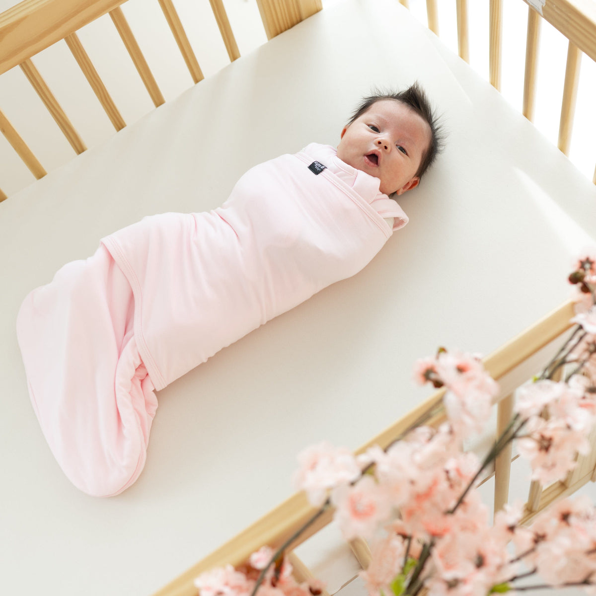 Baby wearing Kyte Baby Sleep Bag Swaddler in Sakura