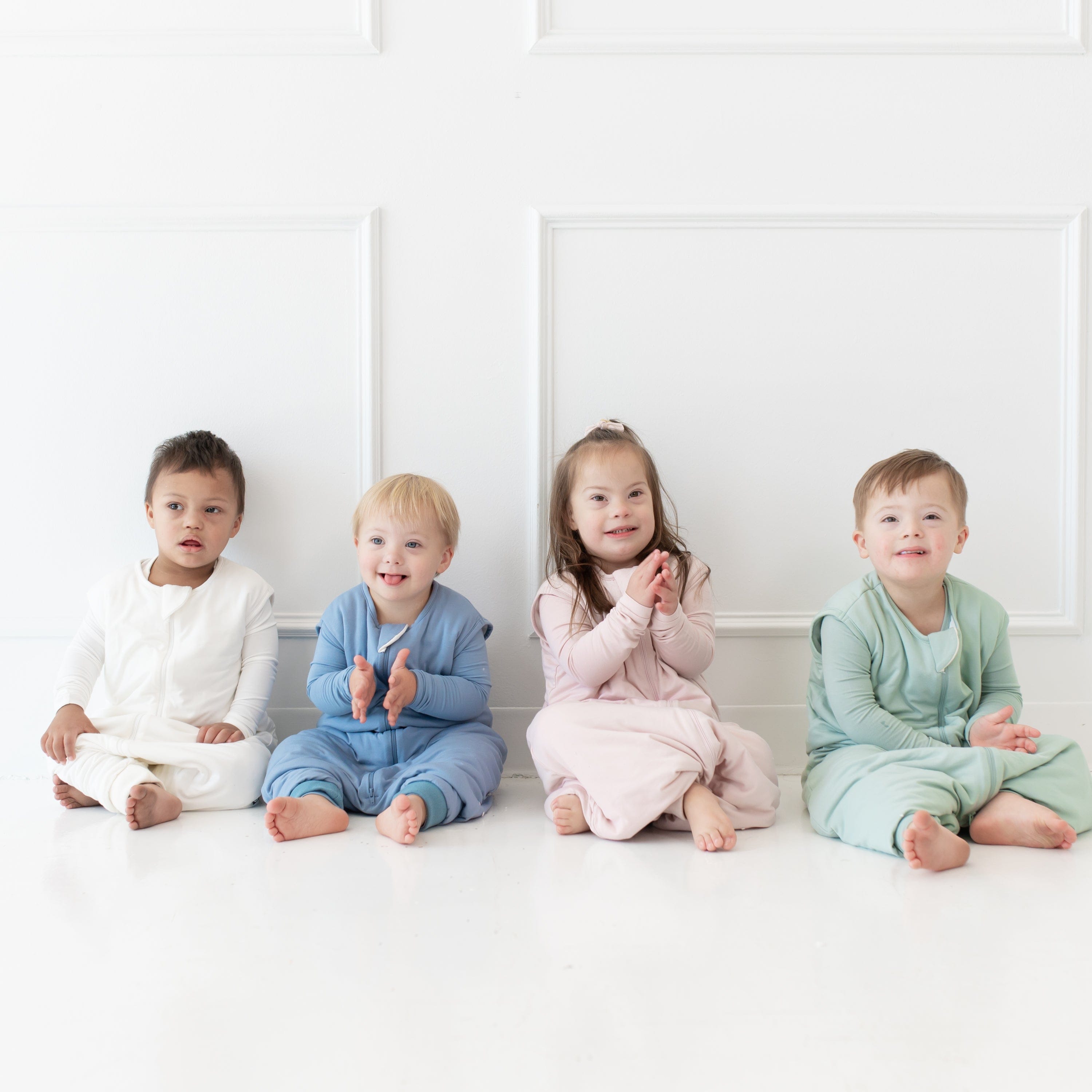 Four sitting toddlers wearing Kyte Baby Sleep Bag Walker 1.0 TOG in Cloud, Slate, Blush and Sage