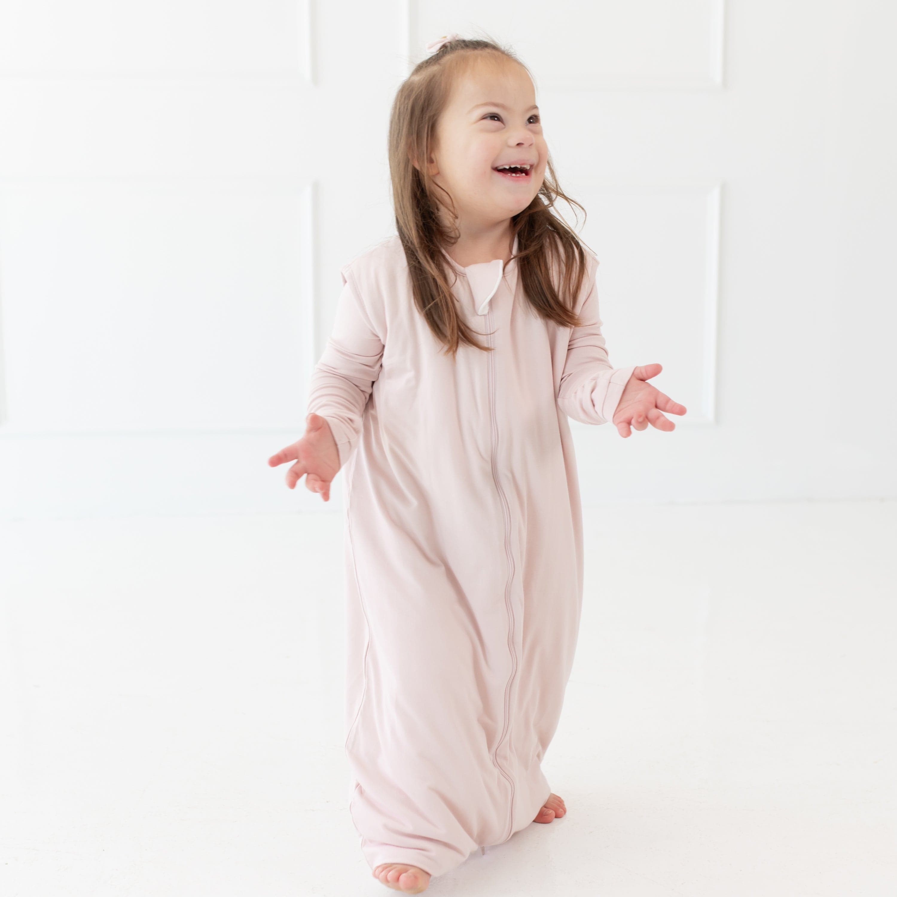 Smiling, standing toddler wearing the Kyte Baby Sleep Bag Walker in Blush 1.0 TOG