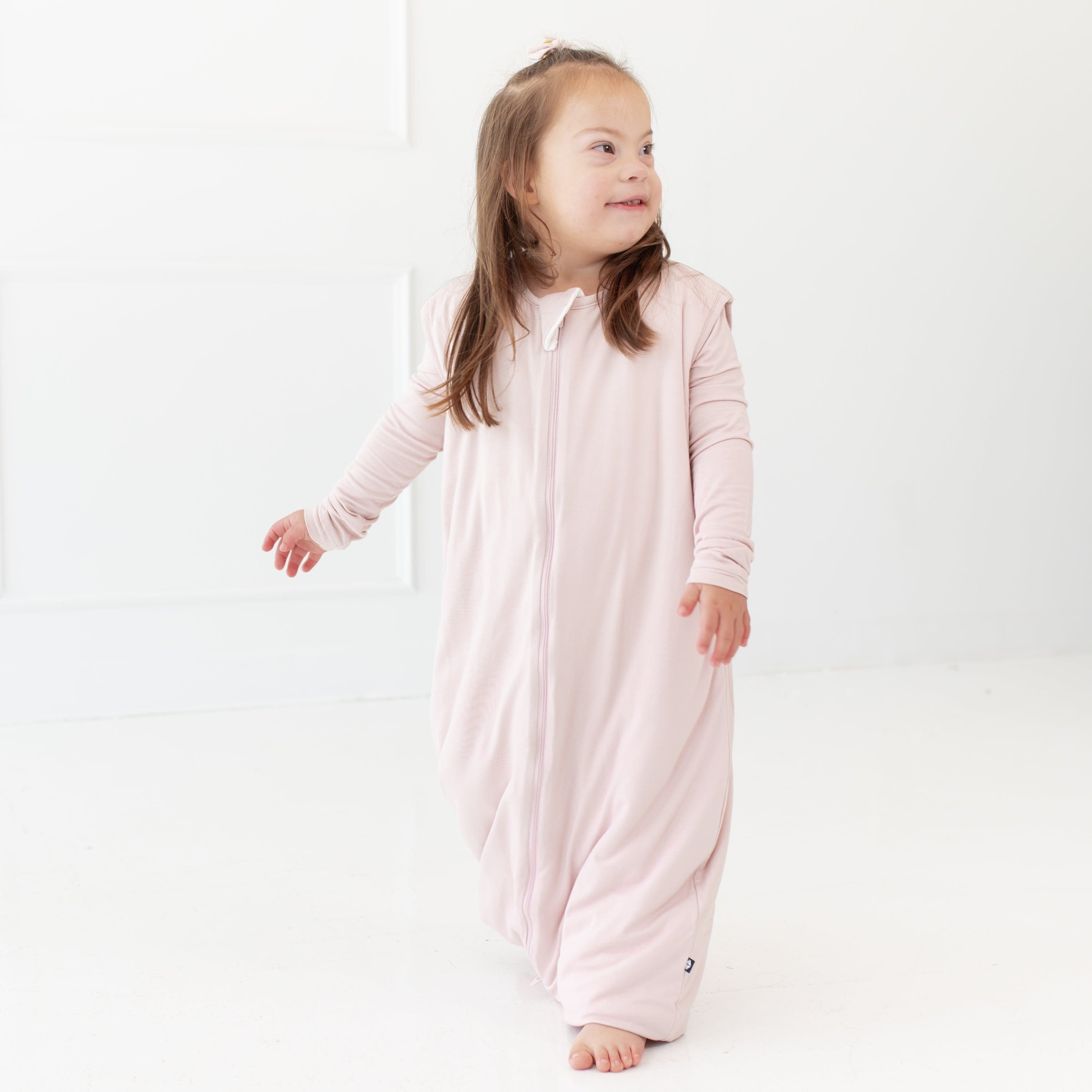 Standing toddler looking to the right hand side while wearing a Kyte Baby Sleep Bag Walker 1.0 in Blush