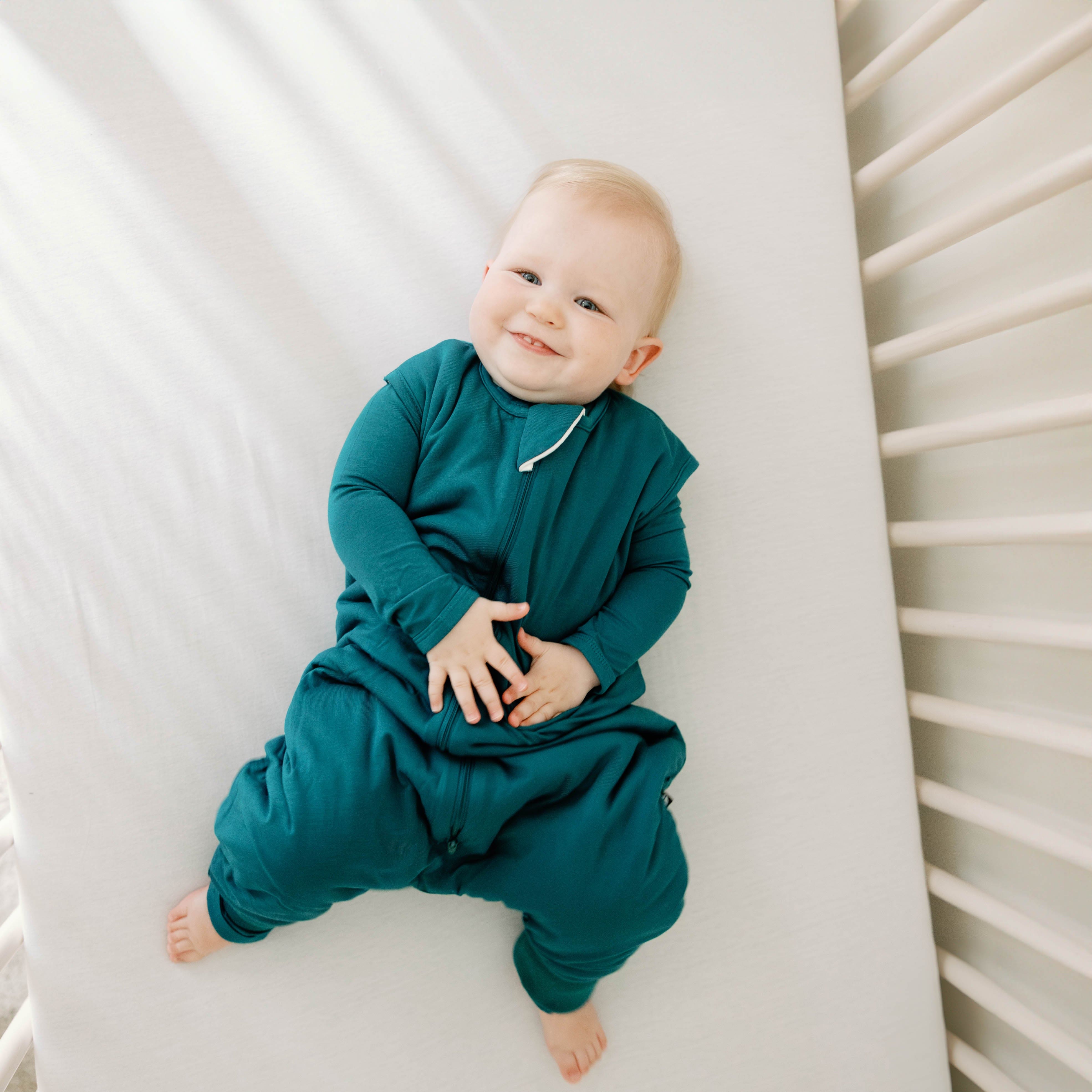 Smiling infant laying in a crib wearing the Sleep Bag Walker in Loch 1.0