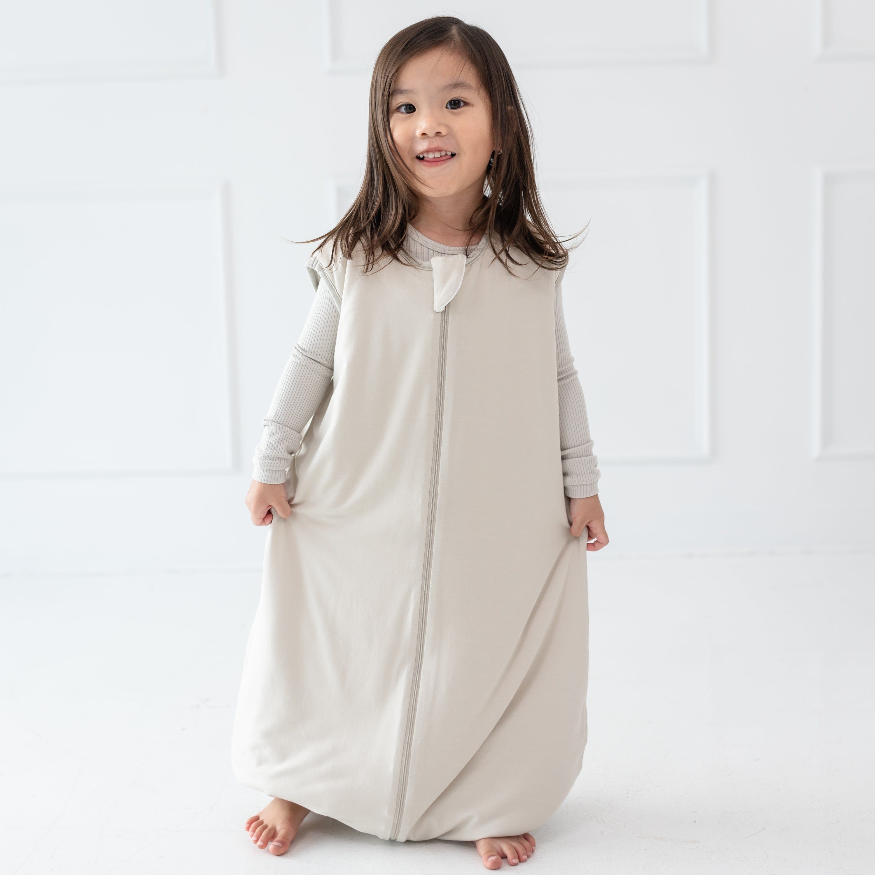 Child model standing wearing the Sleep Bag Walker in Oat 1.0 with matching long sleeve pajamas