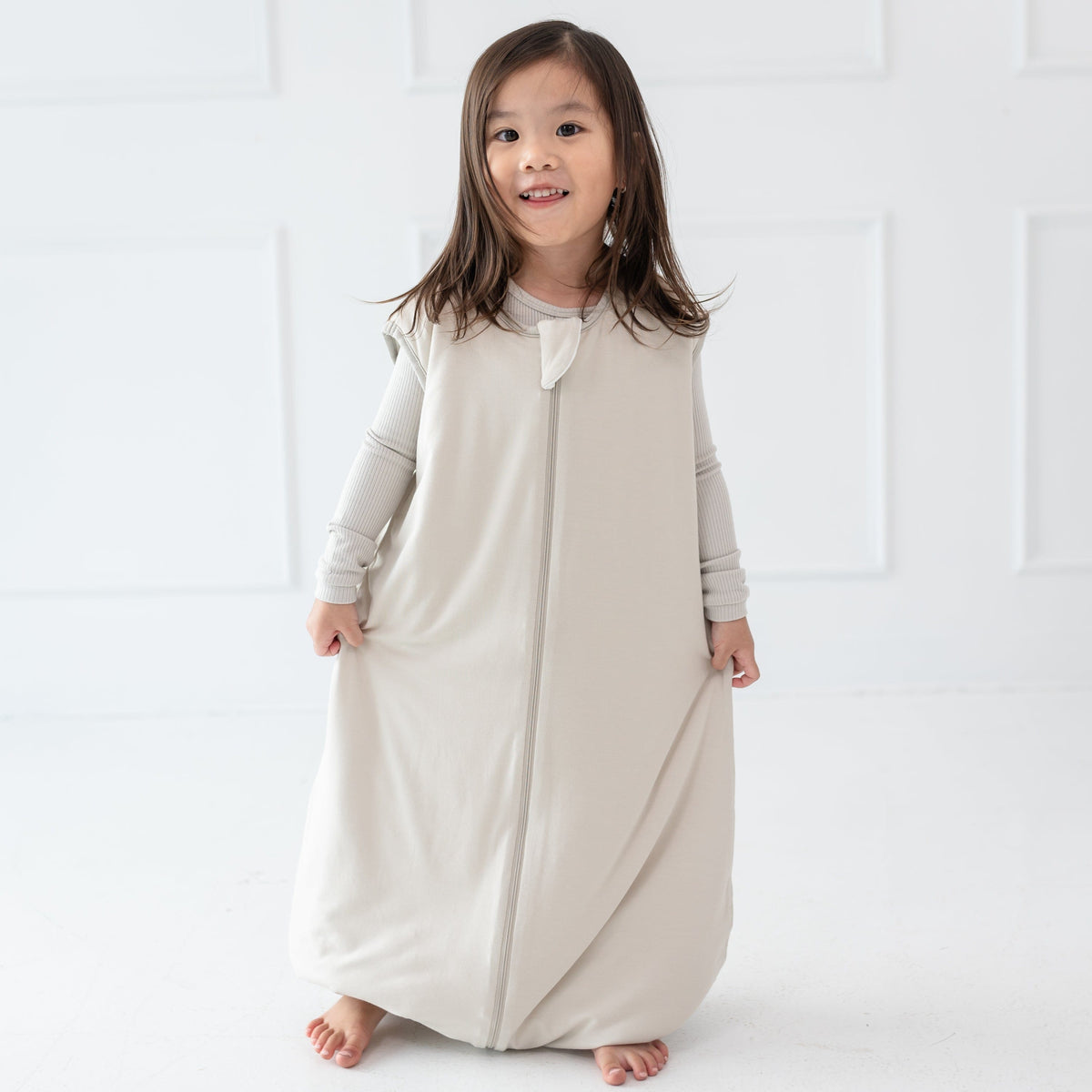 Child model standing wearing the Sleep Bag Walker in Oat 1.0 with matching long sleeve pajamas