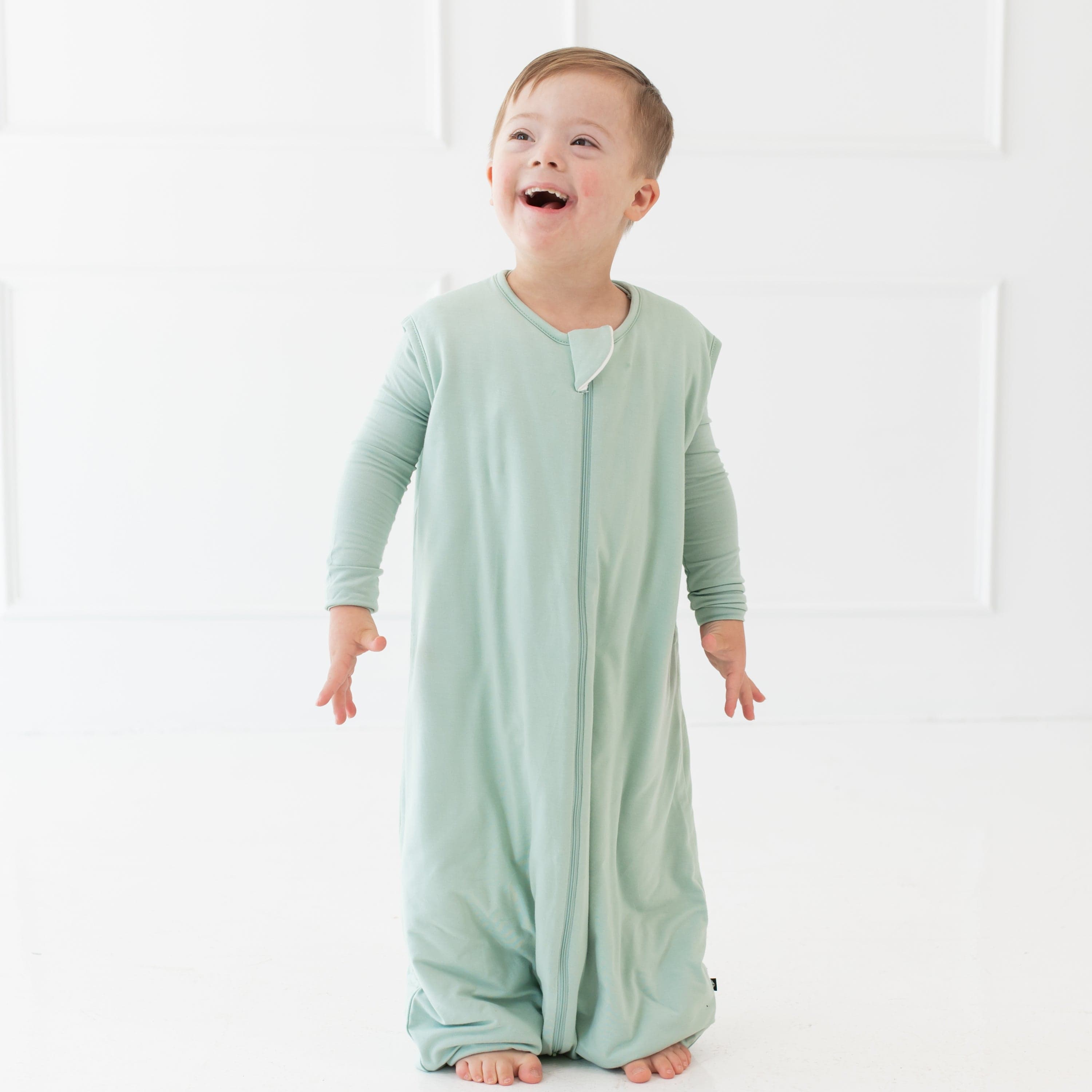 Young smiling child wearing the Sleep Bag Walker in Sage 1.0 with matching long sleeve pajamas