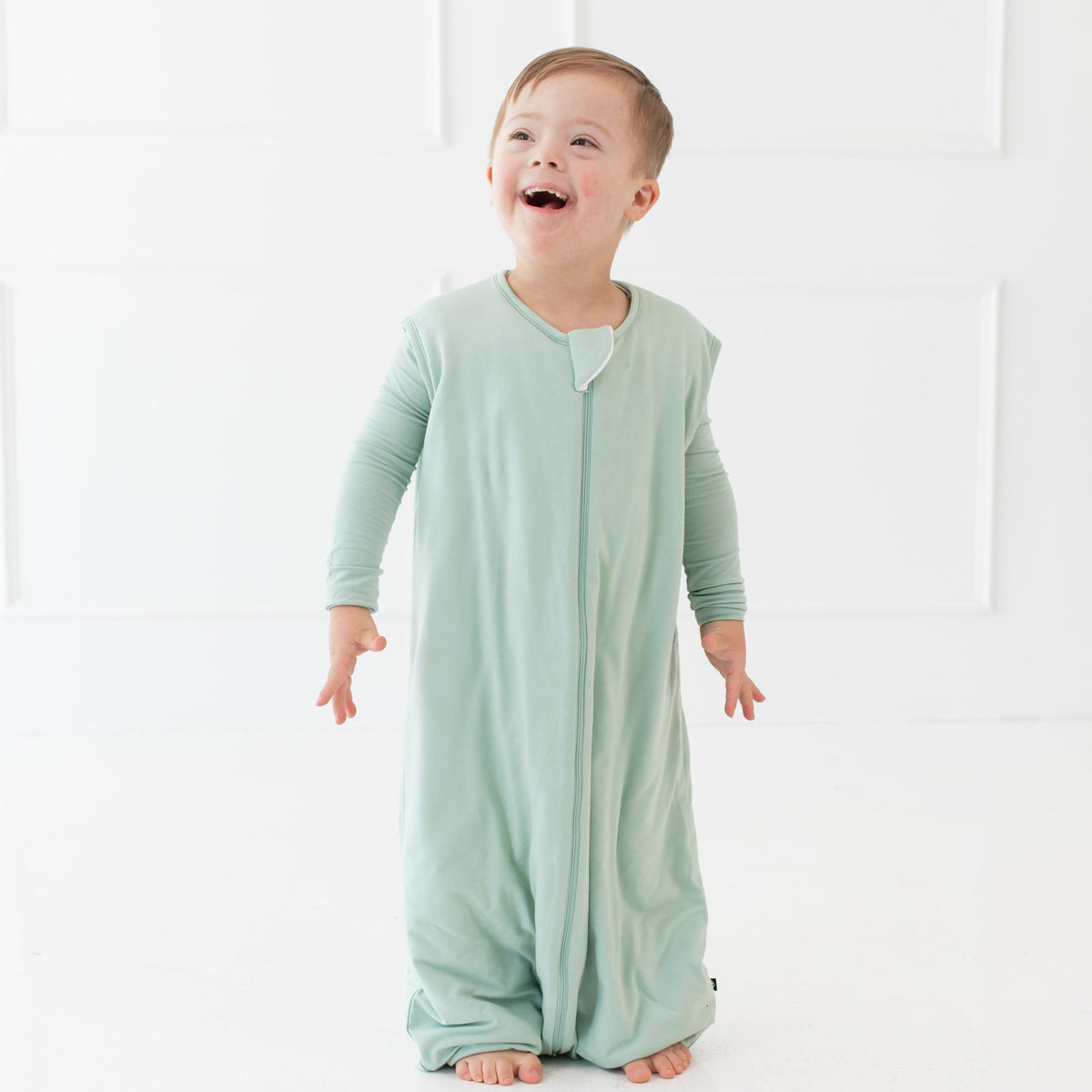 Young smiling child wearing the Sleep Bag Walker in Sage 1.0 with matching long sleeve pajamas