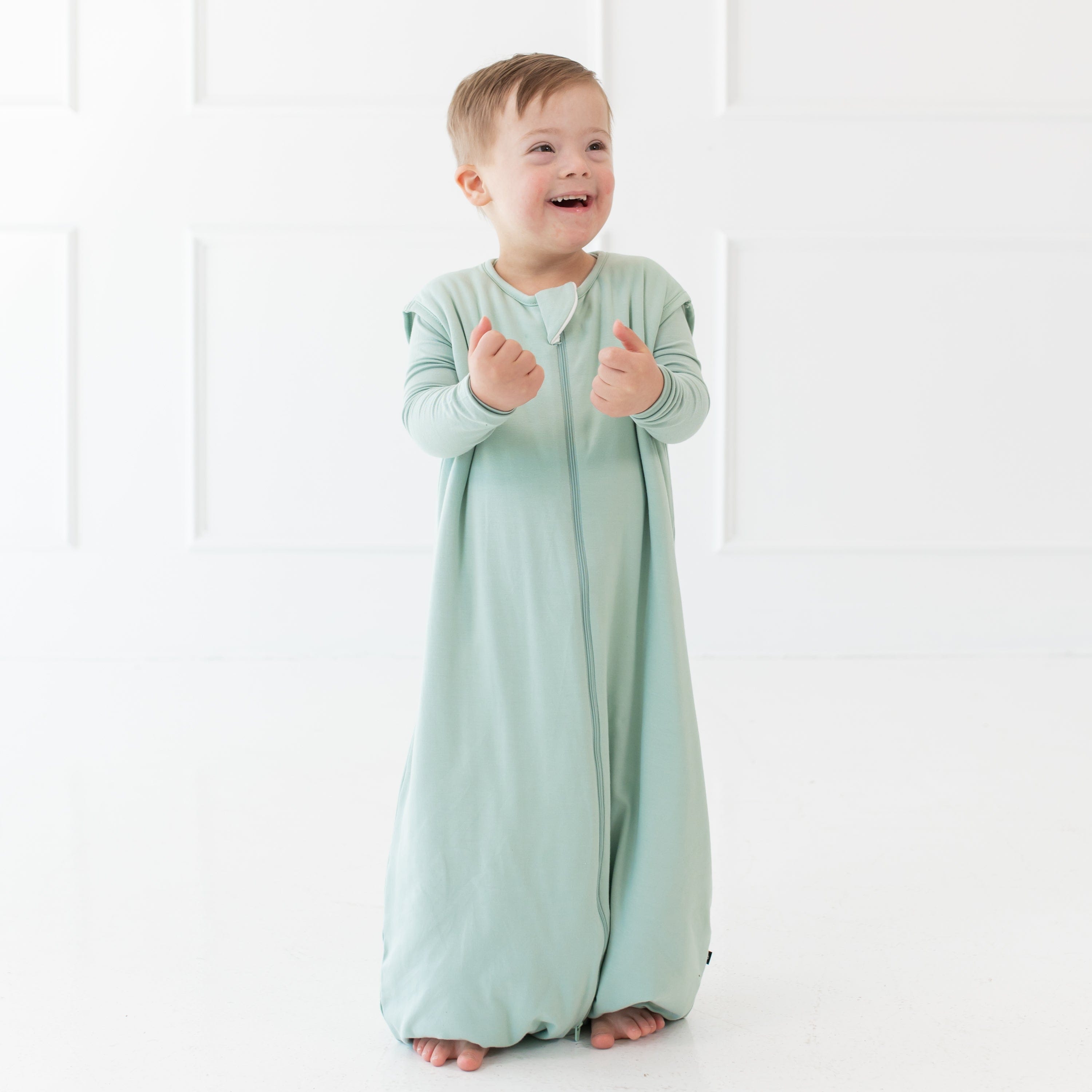 Young smiling child wearing the Sleep Bag Walker in Sage 1.0