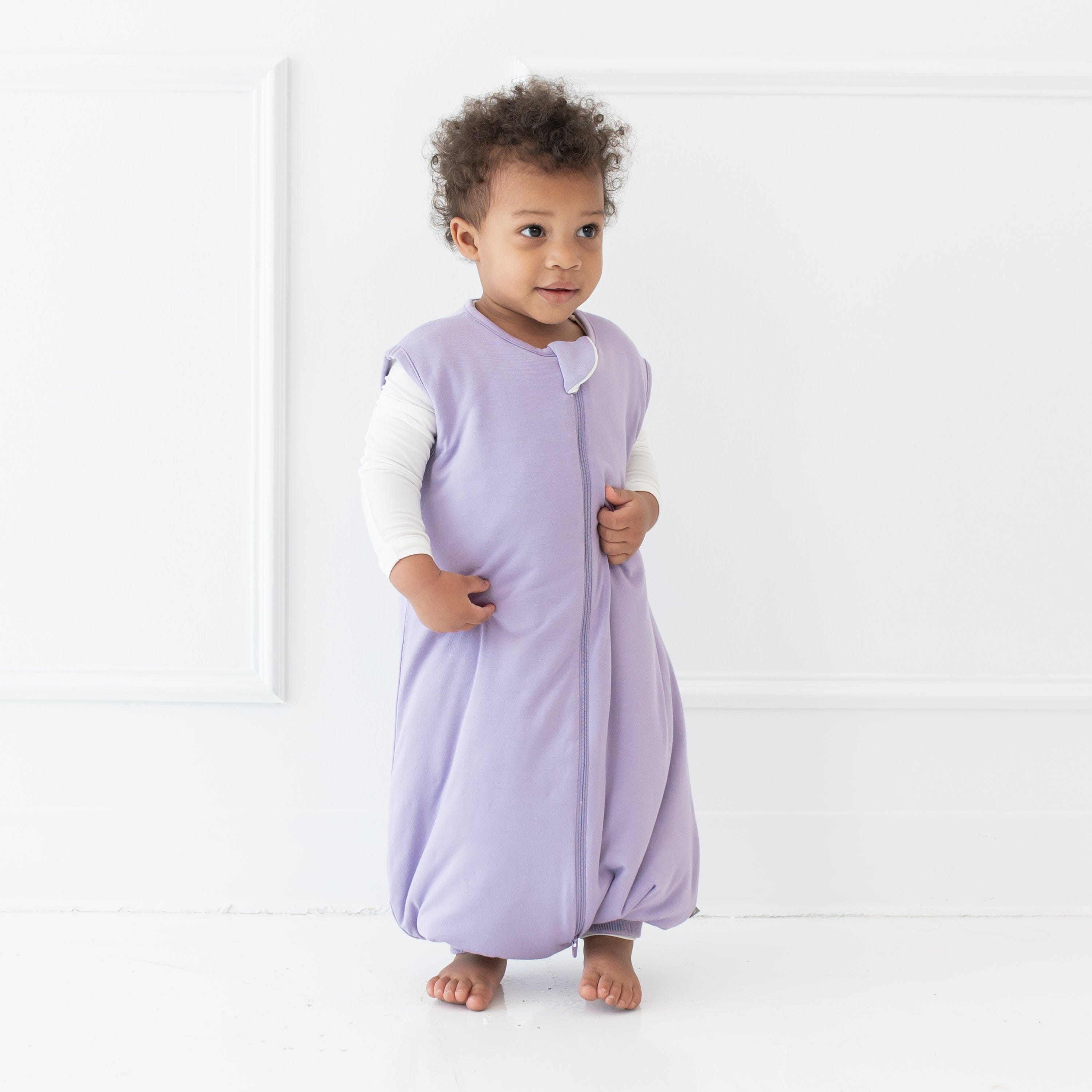 Young model standing looking off to the side wearing the Sleep Bag Walker in Taro 1.0